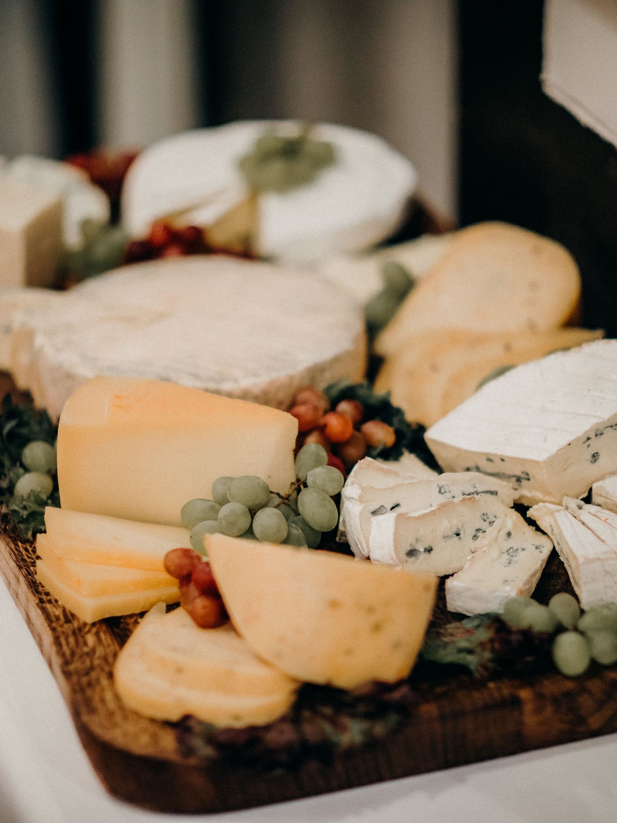 Feine Käseauswahl Holzplatte mit verschiedenen Käsesorten und Trauben als Beilage für einen Gourmet-Aperitif.