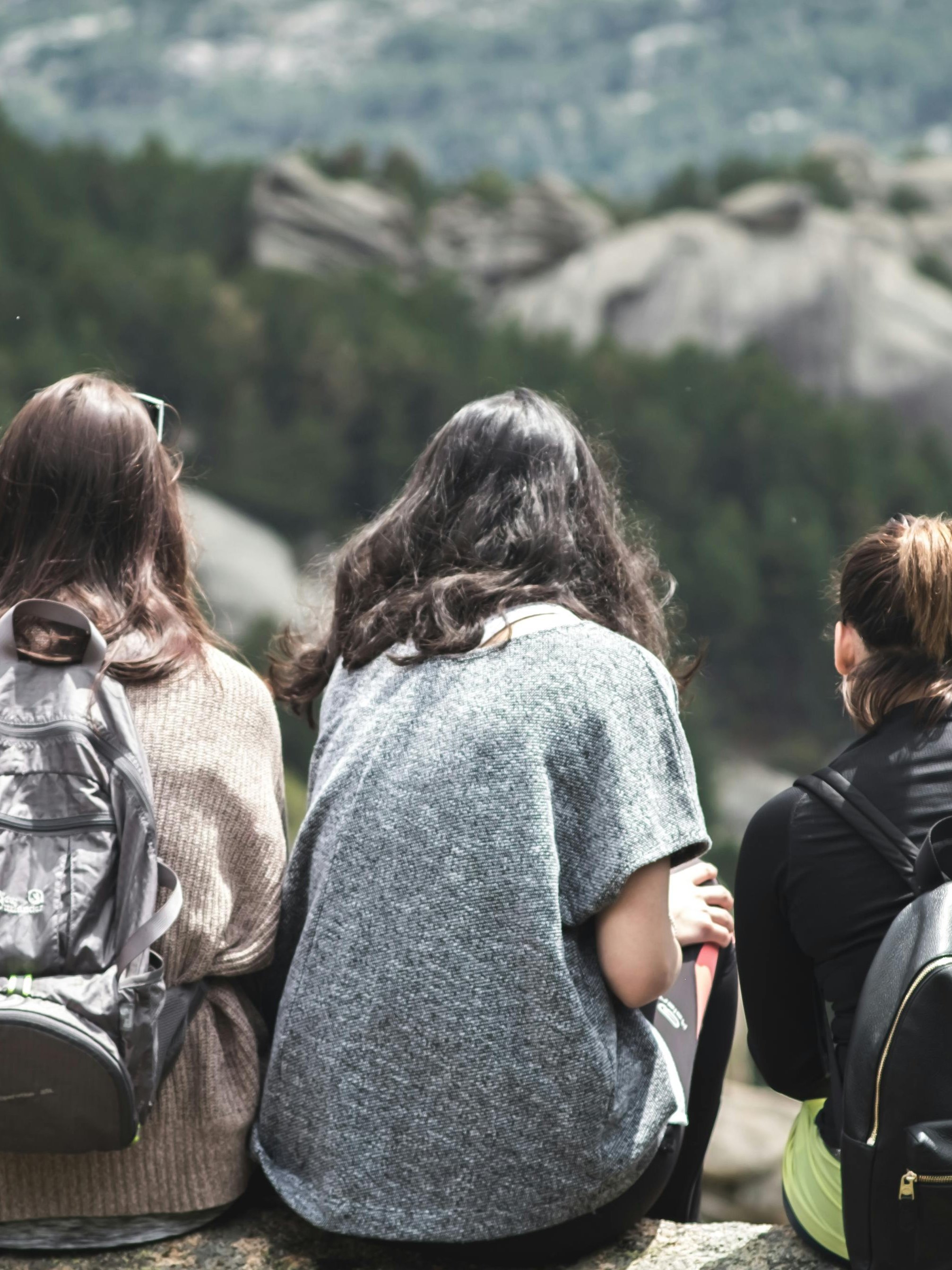Gemeinsame Momente in der Natur Fünf Frauen sitzen auf einem Felsen und blicken auf eine Berglandschaft mit Bäumen im Hintergrund