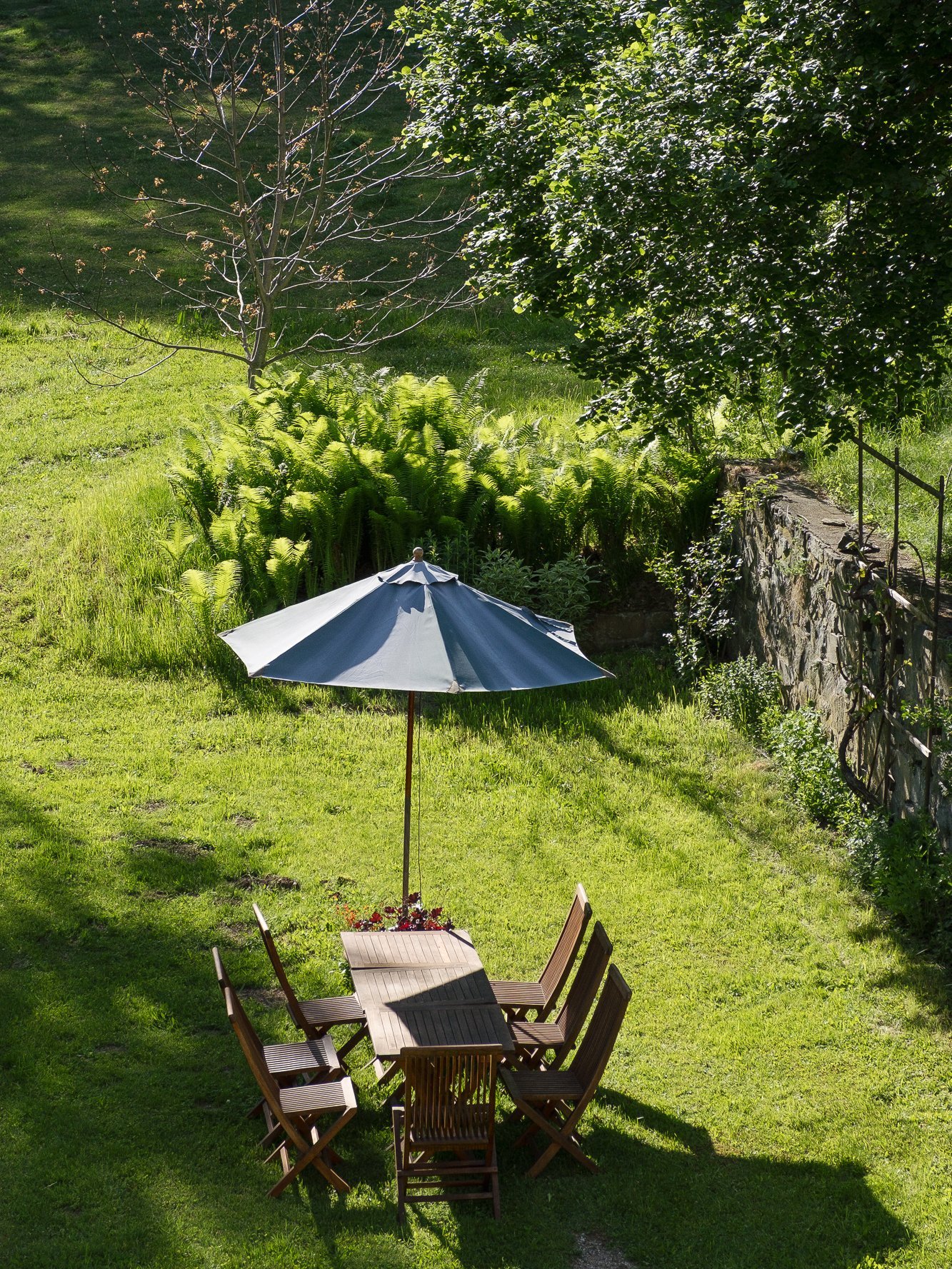 Holztisch und Stühle unter einem großen Sonnenschirm in einer grünen Gartenlandschaft