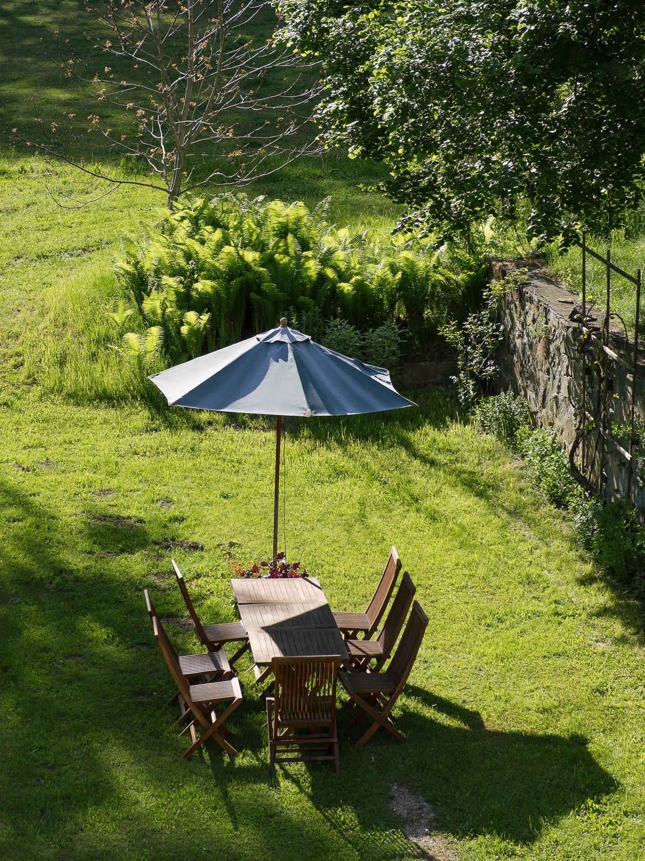 Idyllisches Outdoor-Dining Holztisch und Stühle unter einem großen Sonnenschirm in einer grünen Gartenlandschaft