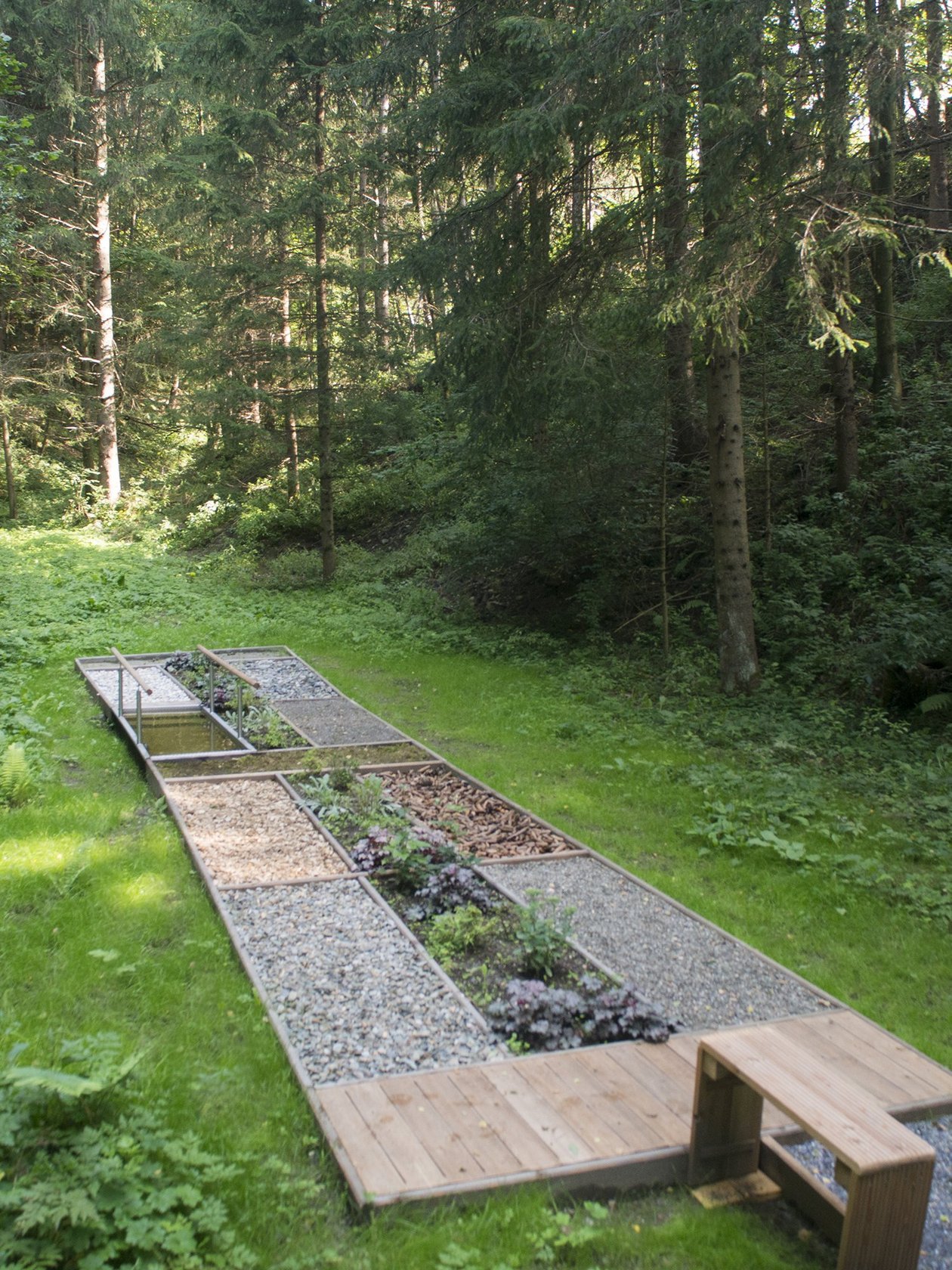 Waldweg mit verschiedenen Materialien und Garten-Elementen umgeben von Bäumen und Pflanzen