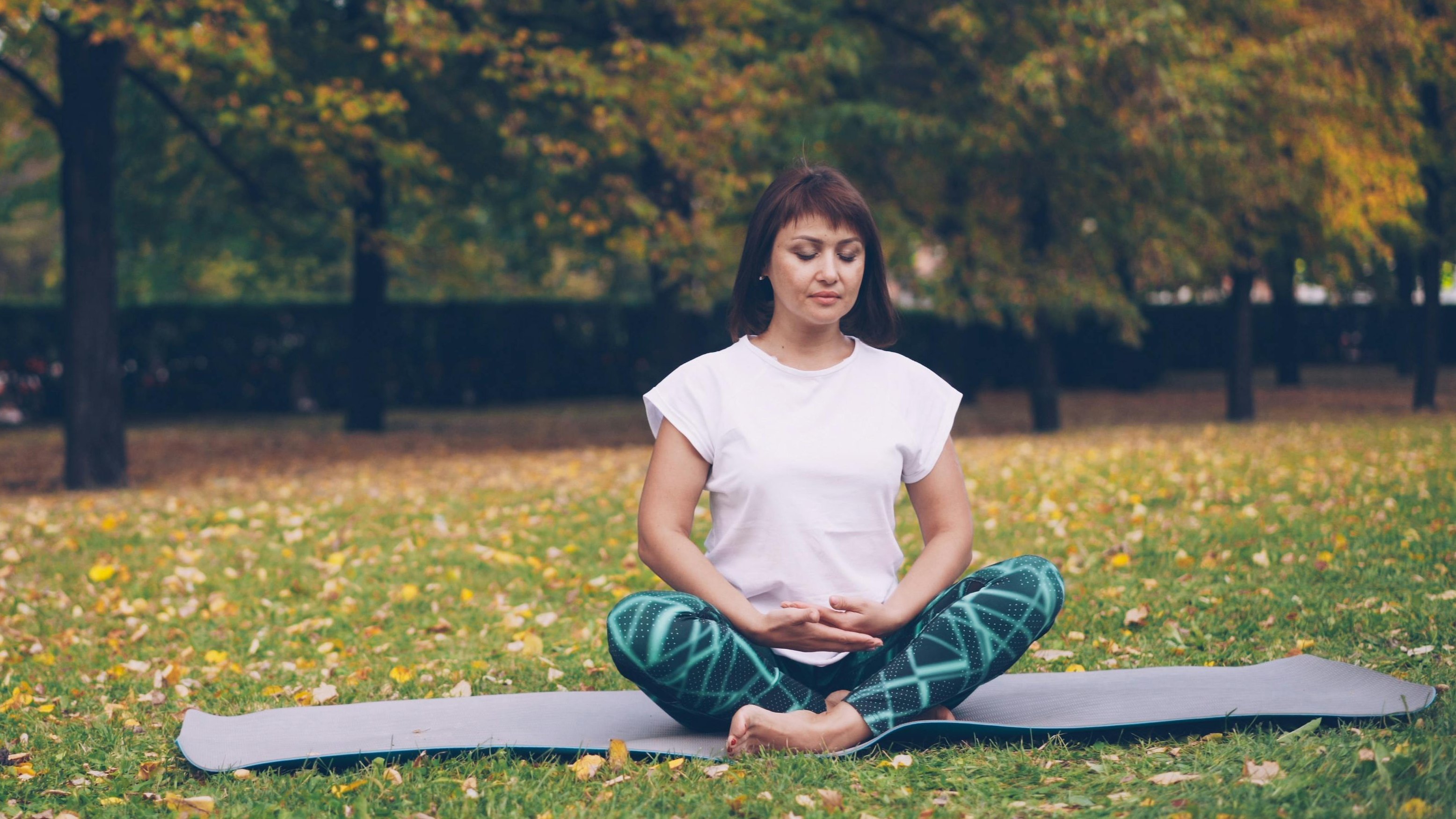 Yoga im Freien Frau praktiziert Yoga in einer ruhigen Umgebung mit Bäumen und Laub auf dem Boden