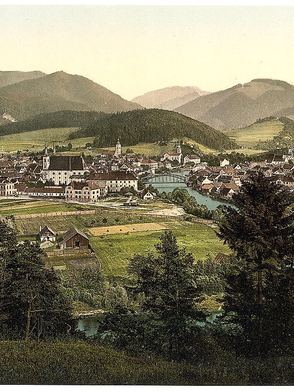 Scenic view of a town by a river surrounded by mountains and greenery in the background
