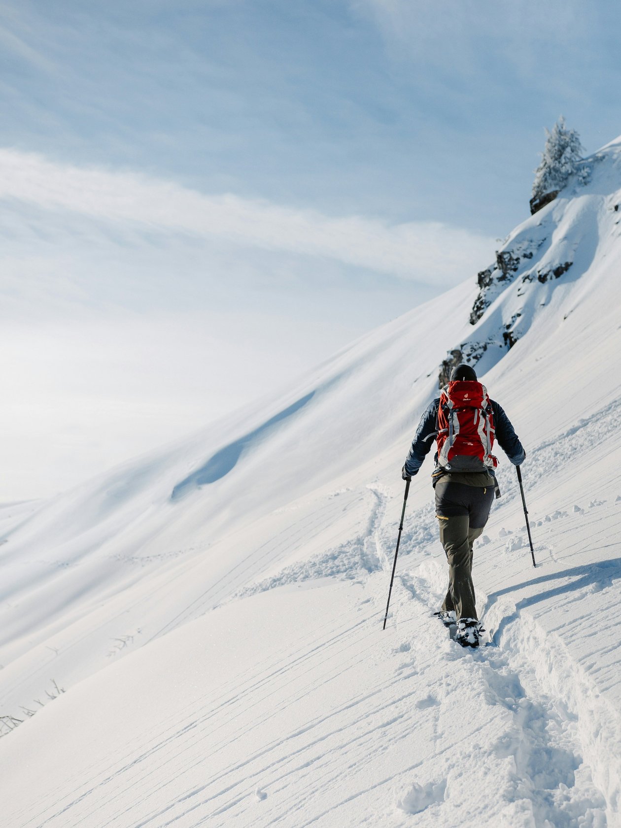 Schneeschuhwanderung in den Bergen Eine Person wandert mit Schneeschuhen auf einem verschneiten Berghang unter blauem Himmel.