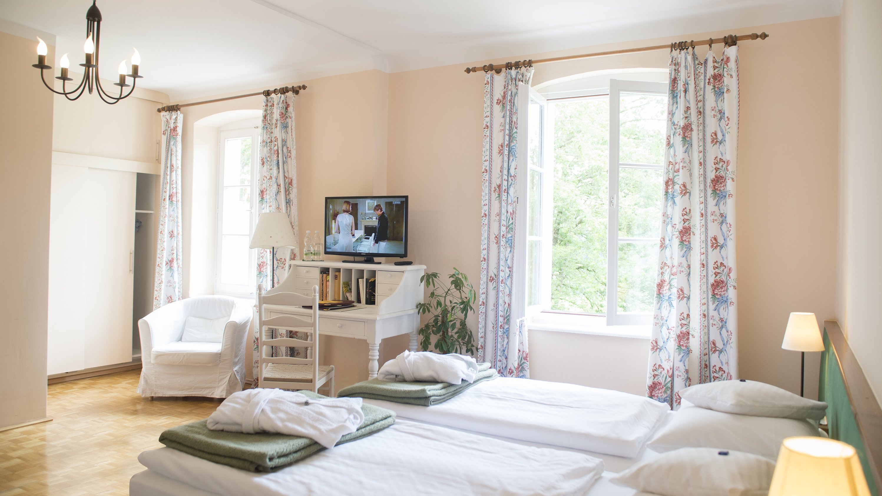 Helles Hotelzimmer mit zwei Betten, Fernseher und Sitzbereich mit Stuhl und Tisch