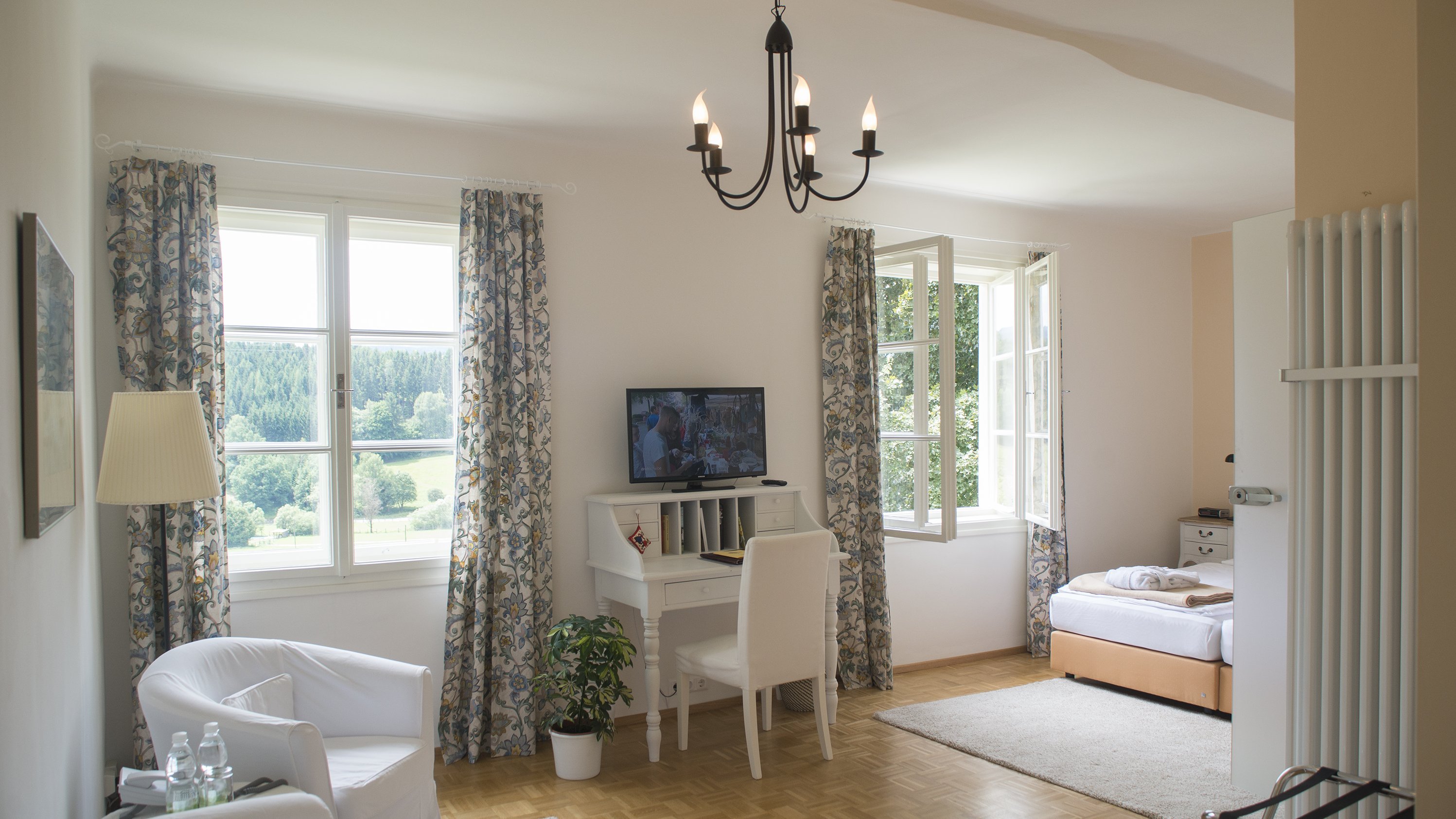 Harmonisches Wohnen im Hotel Landsitz Pischlschloss Heller Wohnbereich mit Stuhl, Schreibtisch und Fernseher, Schlafzimmer im Hintergrund
