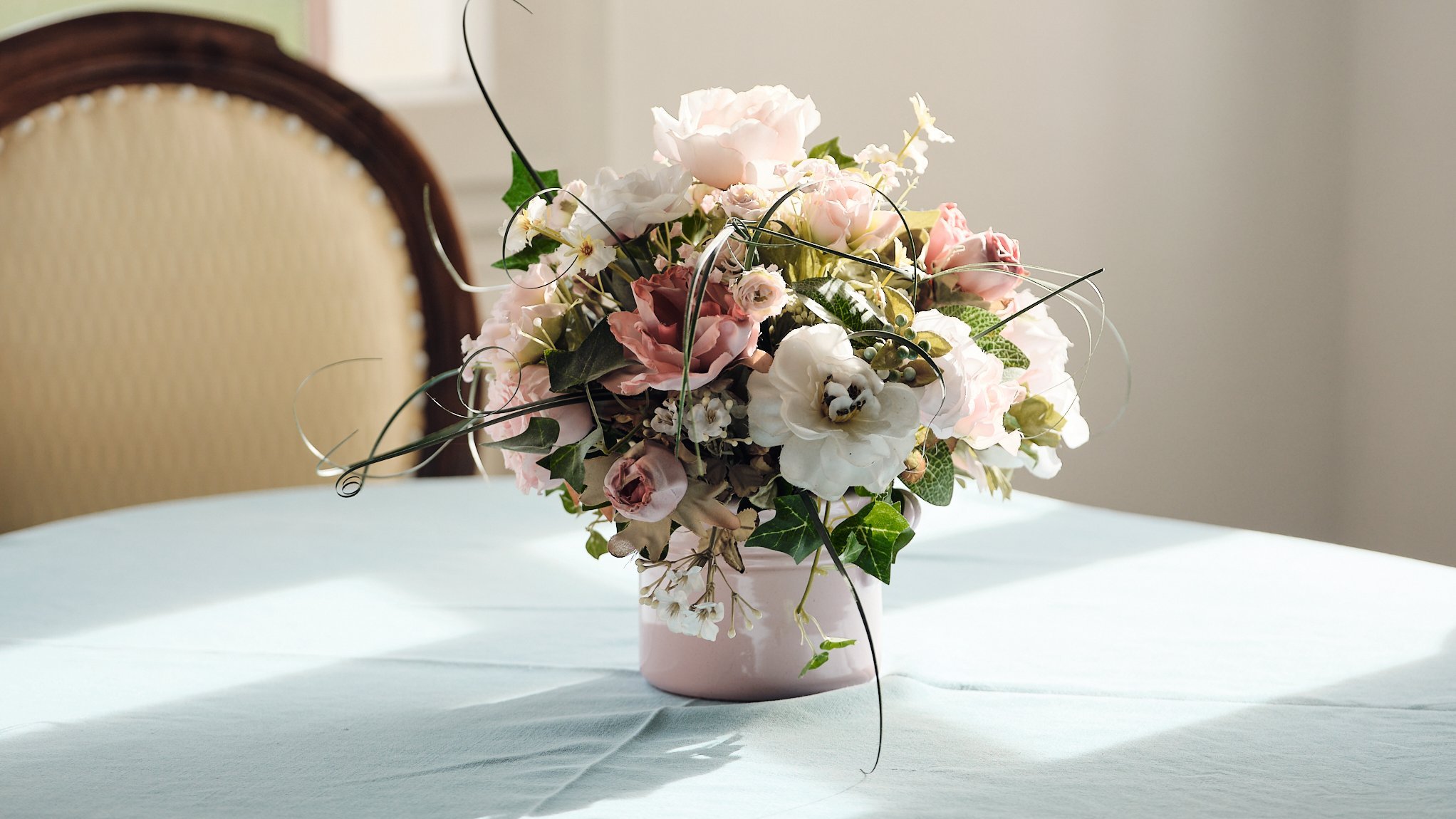 Florale Eleganz für jeden Anlass Dekorative Blumenarrangement in einer rosa Vase auf einem hellblauen Tischdecken.
