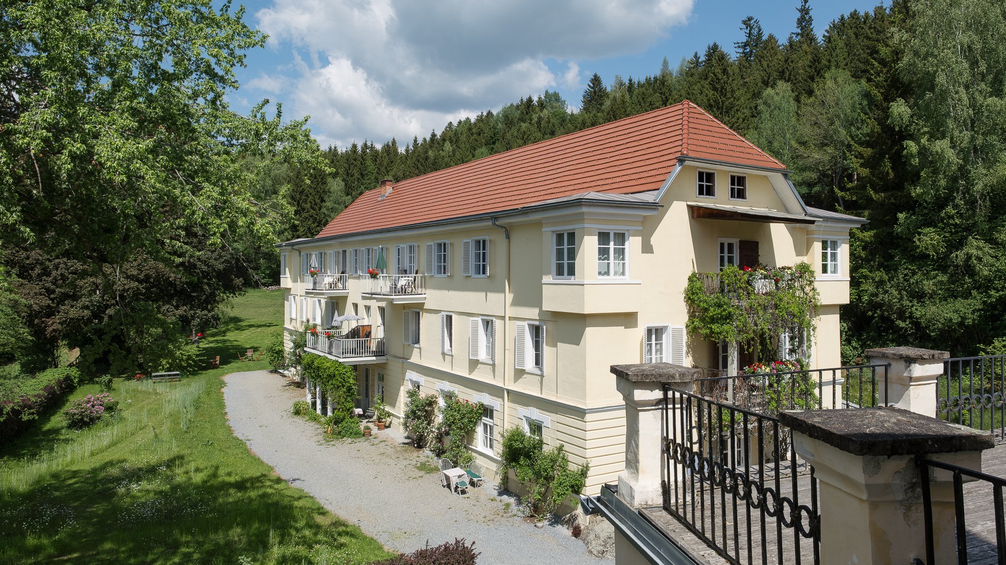 Landsitz Pichlschloss in der Natur Großes, Wohngebäude umgeben von Bäumen und Grünflächen, mit einem Kiesweg davor.