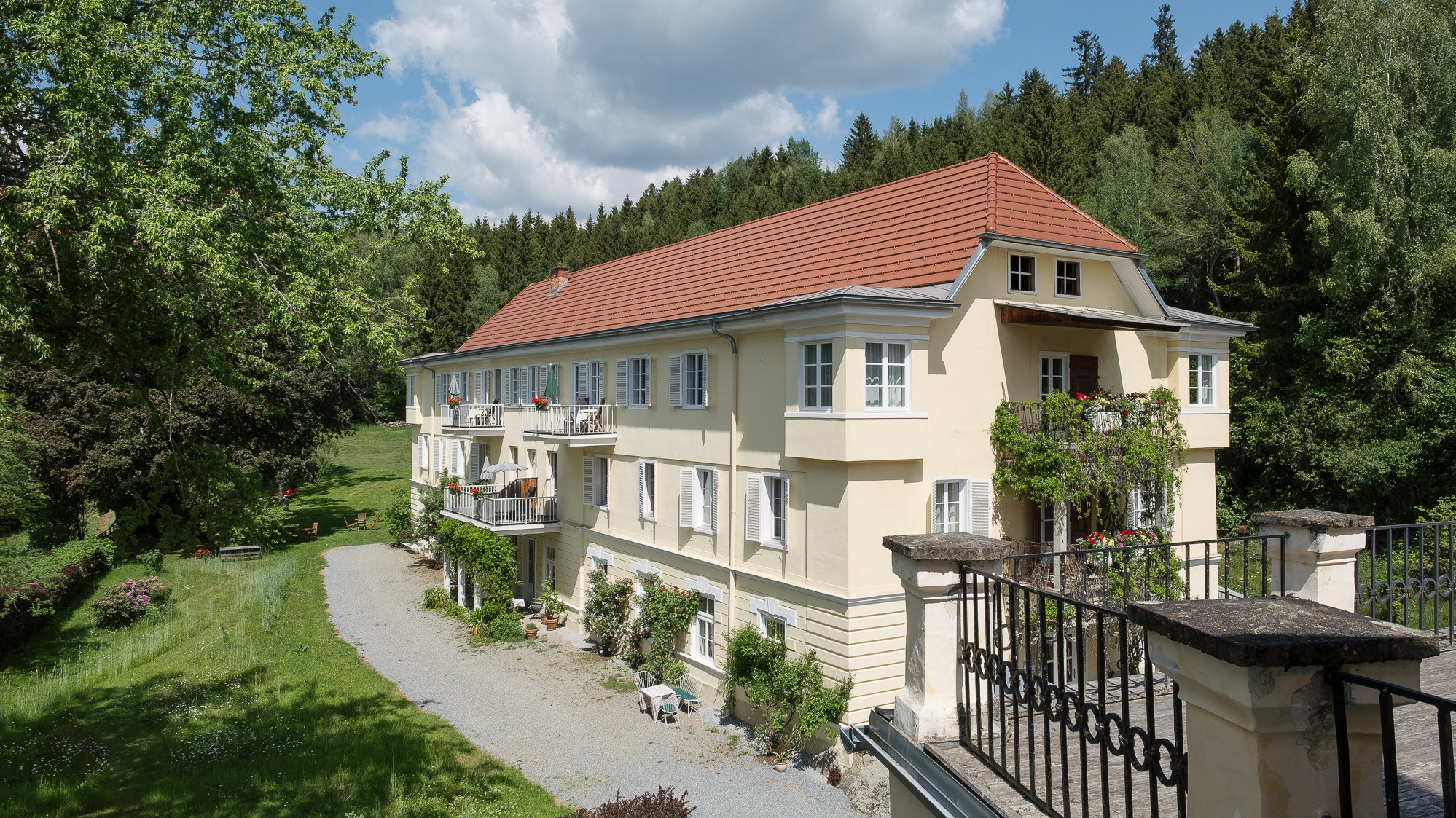 Pichlschloss Country Estate in the countryside A large residential building surrounded by trees and green spaces, with a gravel path in front of it.