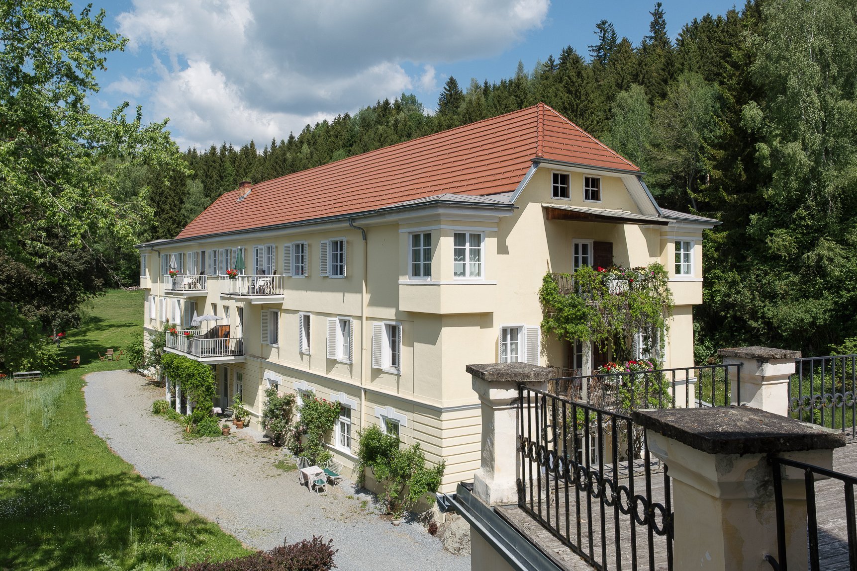Großes, Wohngebäude umgeben von Bäumen und Grünflächen, mit einem Kiesweg davor.