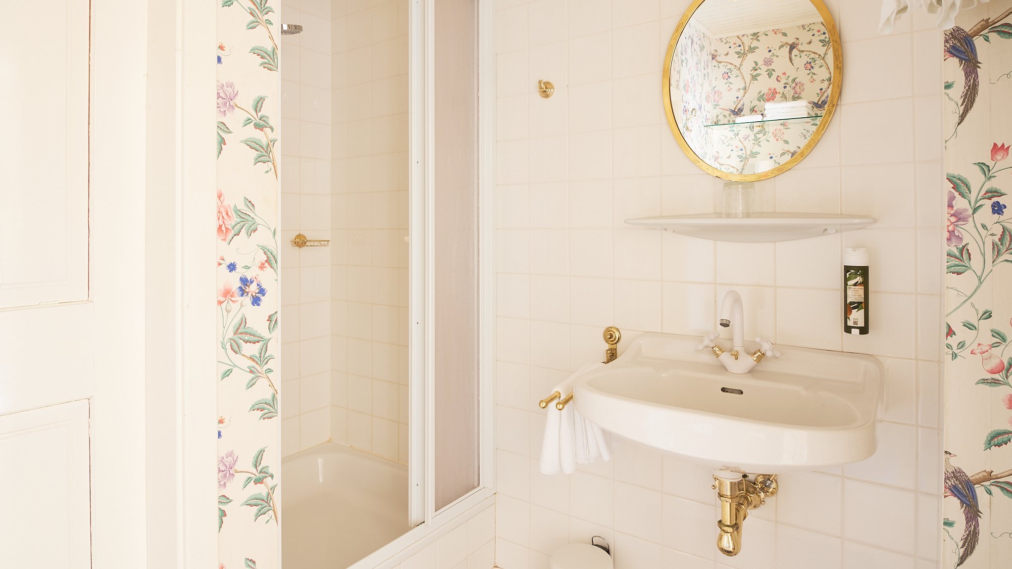 Elegantes Badezimmer mit blumiger Note Badezimmer mit Duschkabine, runder Spiegel und Waschbecken, floralem Tapetendesign