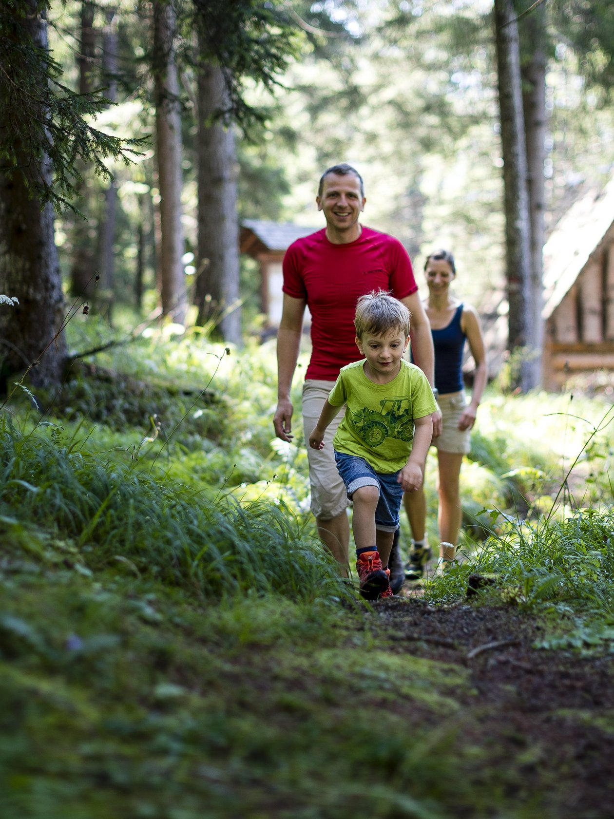 Familienwanderung im Wald Familie wandert durch einen bewaldeten Bereich mit einer Hütte im Hintergrund, ein Kind führt den Weg.
