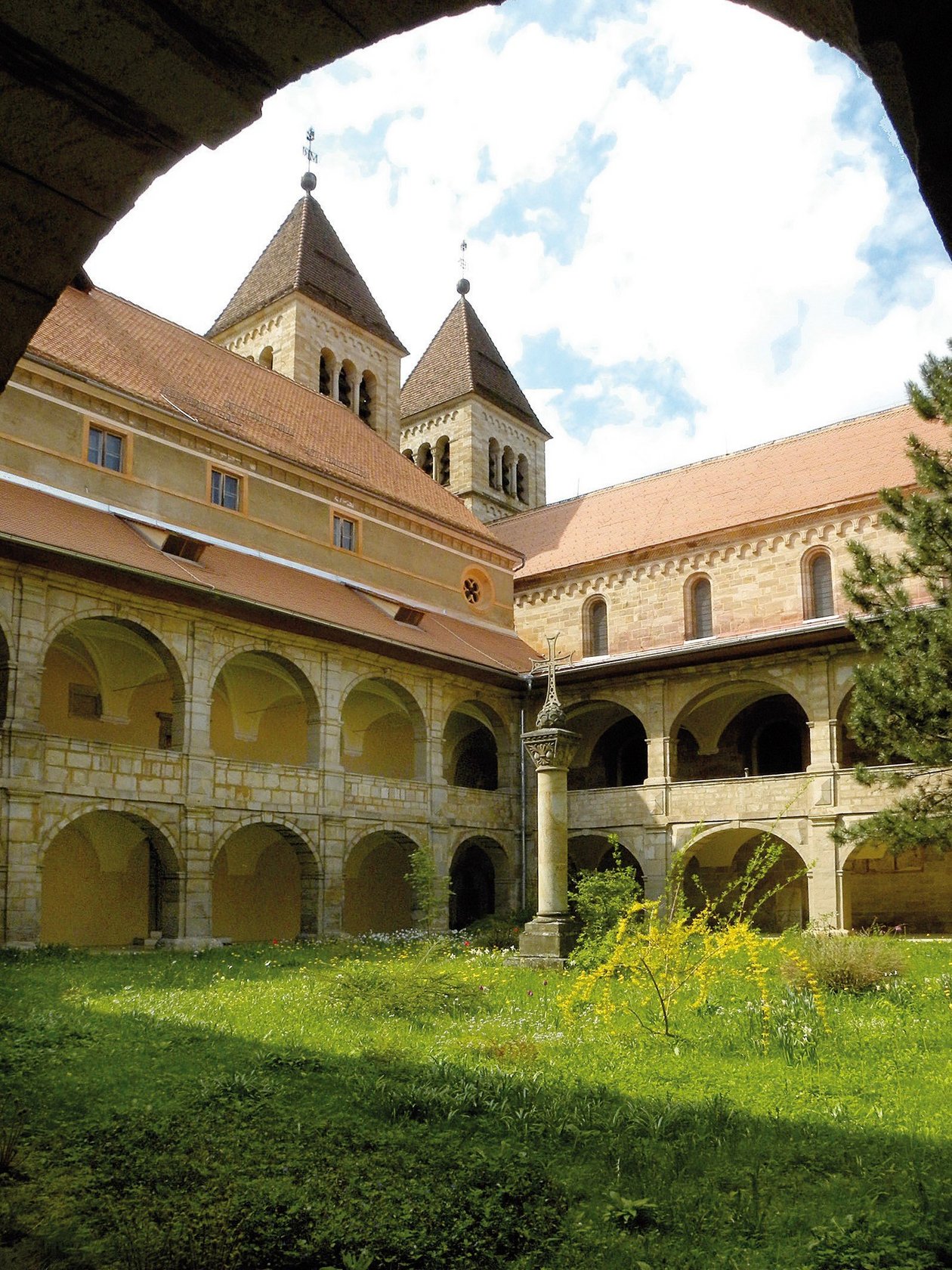 Historische Klosterarchitektur im Innenhof Innenhof eines Klosters mit Bögen und einem Steinsäulen, zwei Türmen im Hintergrund