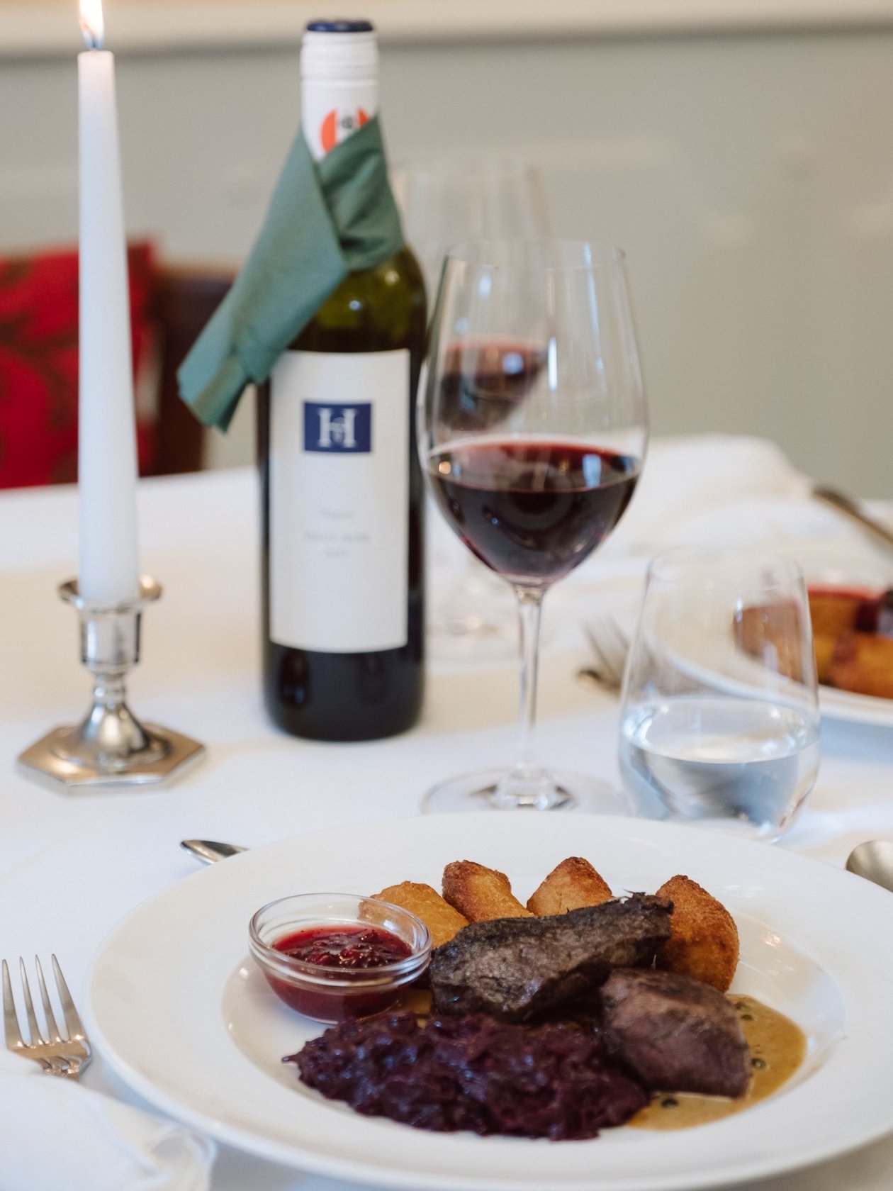 Elegantes Tischgedeck mit Gourmetessen, Rotwein und brennender Kerze für ein kulinarisches Erlebnis