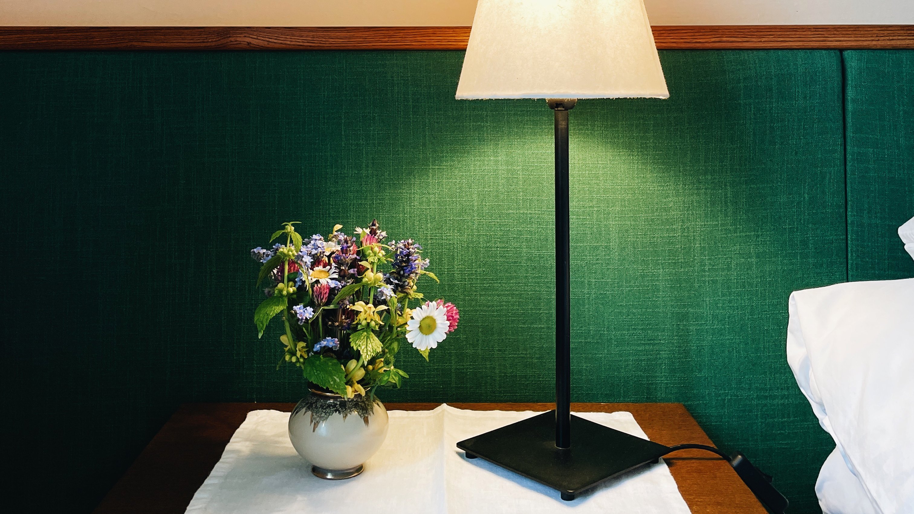 Stilvolle Schlafzimmergestaltung mit Blumen Nachttisch mit Lampe und Blumenvasen auf einer grünen Wand im Schlafzimmerbereich
