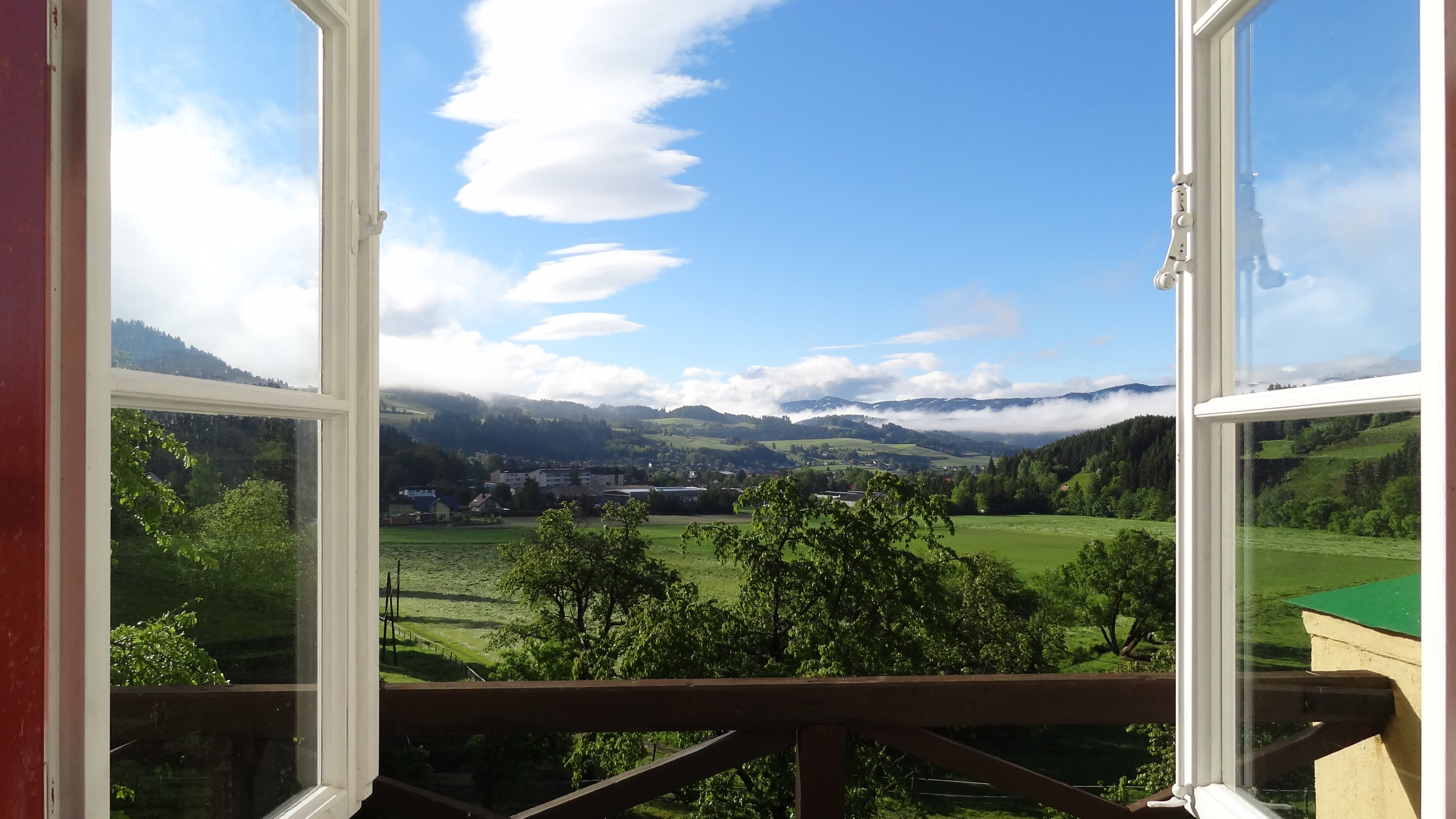 Breathtaking mountain views from an open window Open window revealing a scenic landscape with mountains and greenery under a blue sky