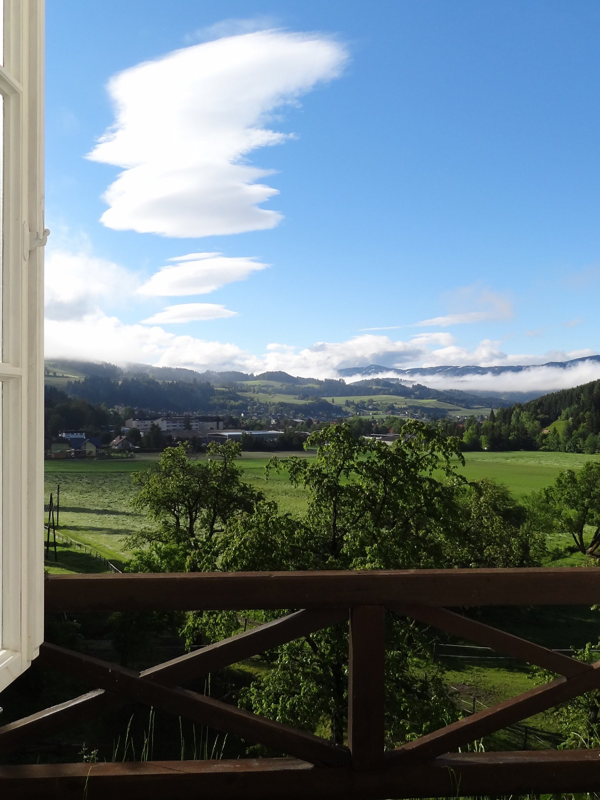 Ein offenes Fenster mit Blick auf eine grüne Landschaft und Berge unter blauem Himmel
