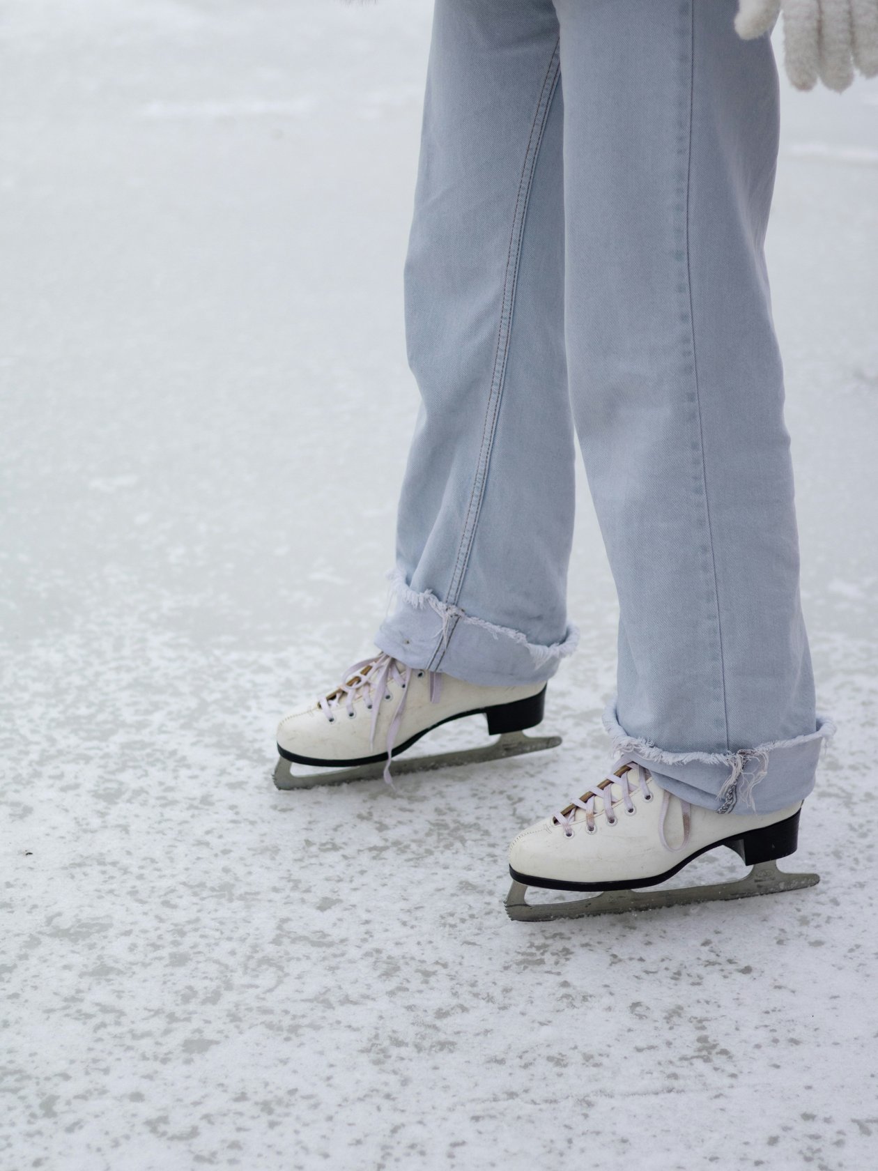 Eislaufen im Winterzauber Personenbeine in blauen Jeans mit weißen Schlittschuhen auf einer eisigen Fläche