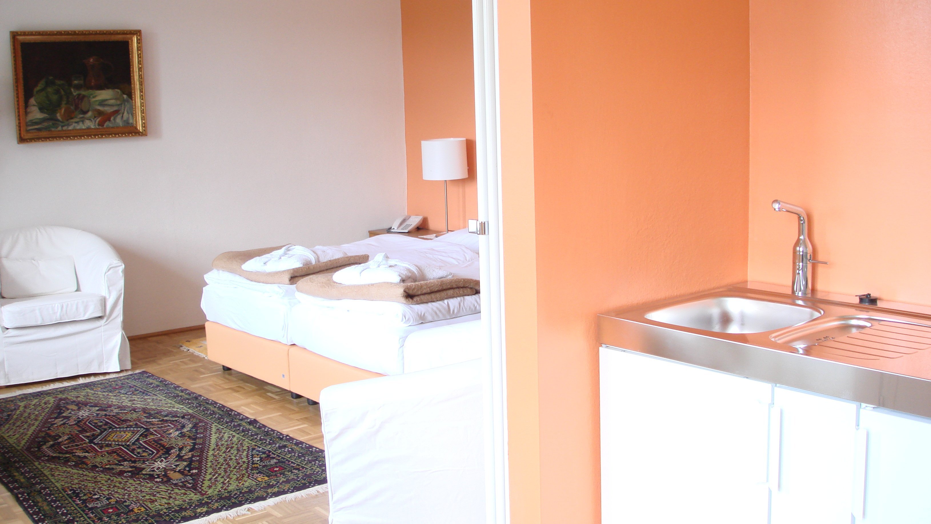 Elegantes Zimmer für erholsame Nächte Hotelzimmer mit Bett, kleiner Küchenzeile und Sitzbereich mit weißem Stuhl, gemütliche Inneneinrichtung.
