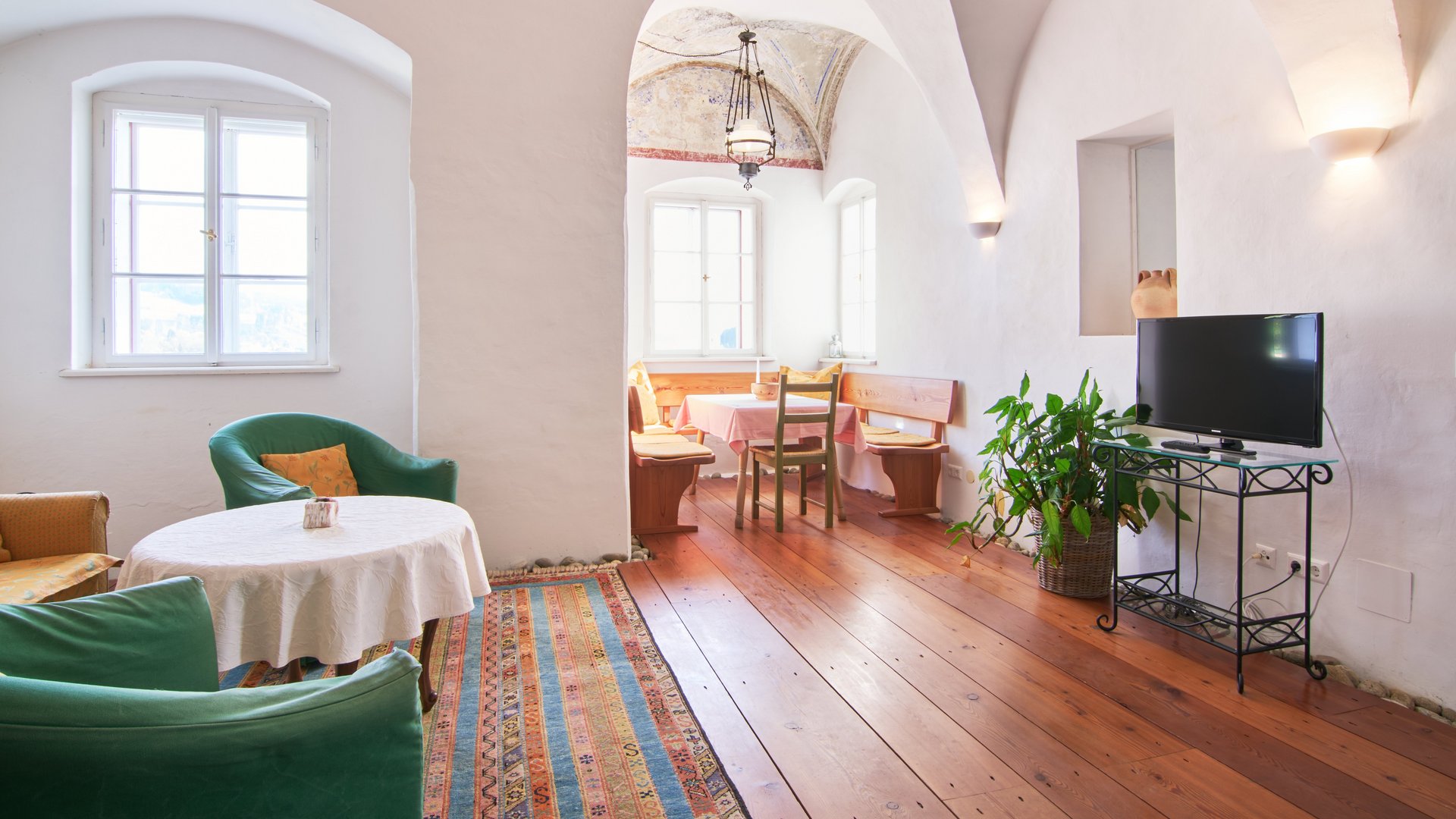 Gemütliches Wohnzimmer mit hohen gewölbten Decken, grünen Stühlen und einem Tisch