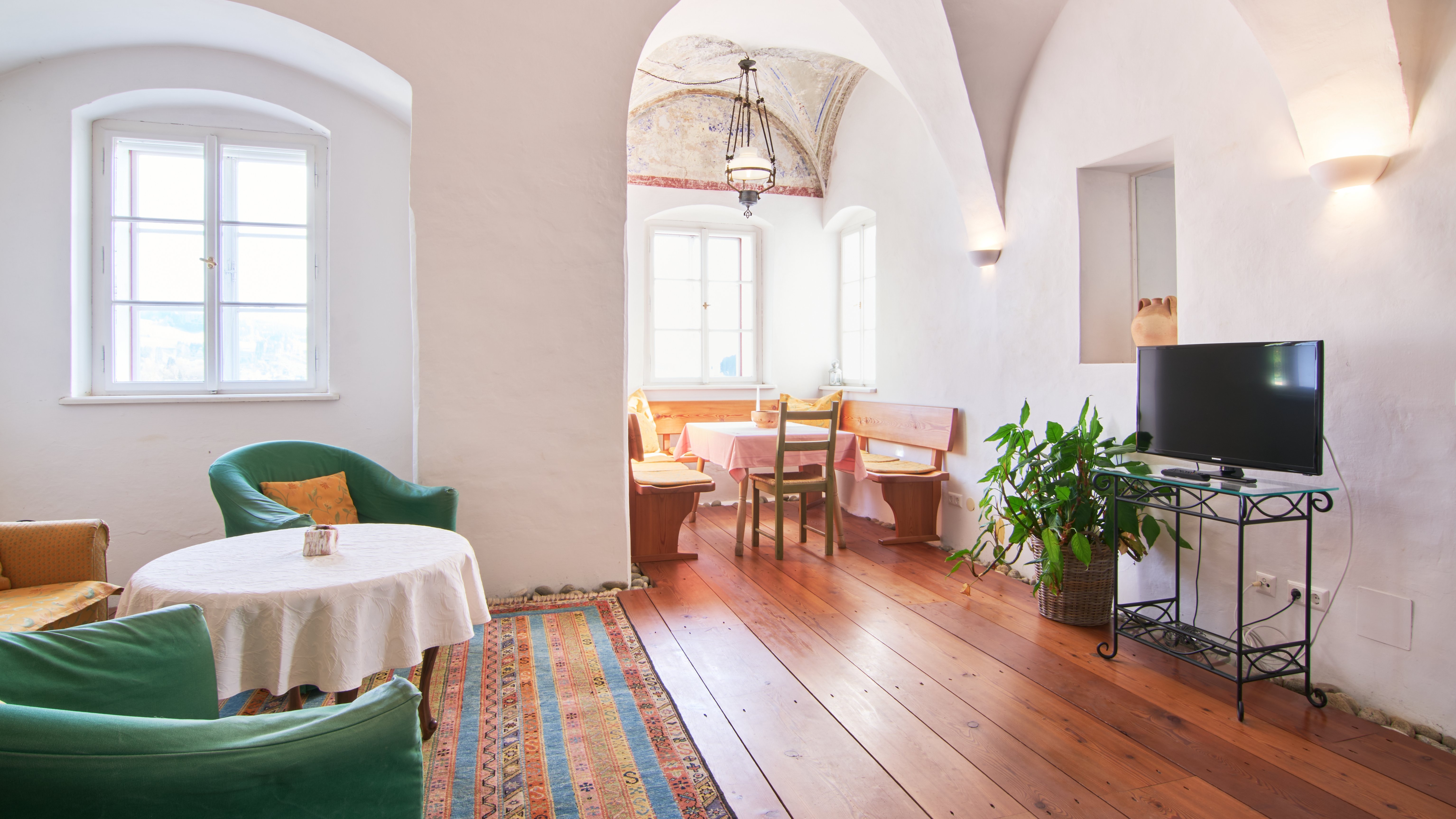 Gemütliches Wohnzimmer mit hohen gewölbten Decken, grünen Stühlen und einem Tisch