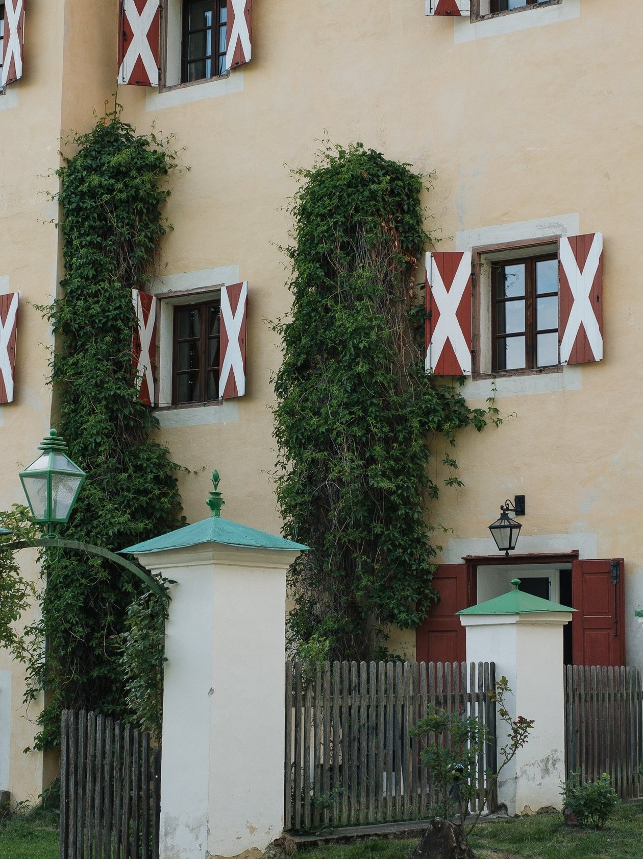 Historisches Fassade des Pichlschloss Fassade des Pichlschloss, mit roten und weißen Fensterläden, umgeben von Pflanzen und einem Holzzaun.