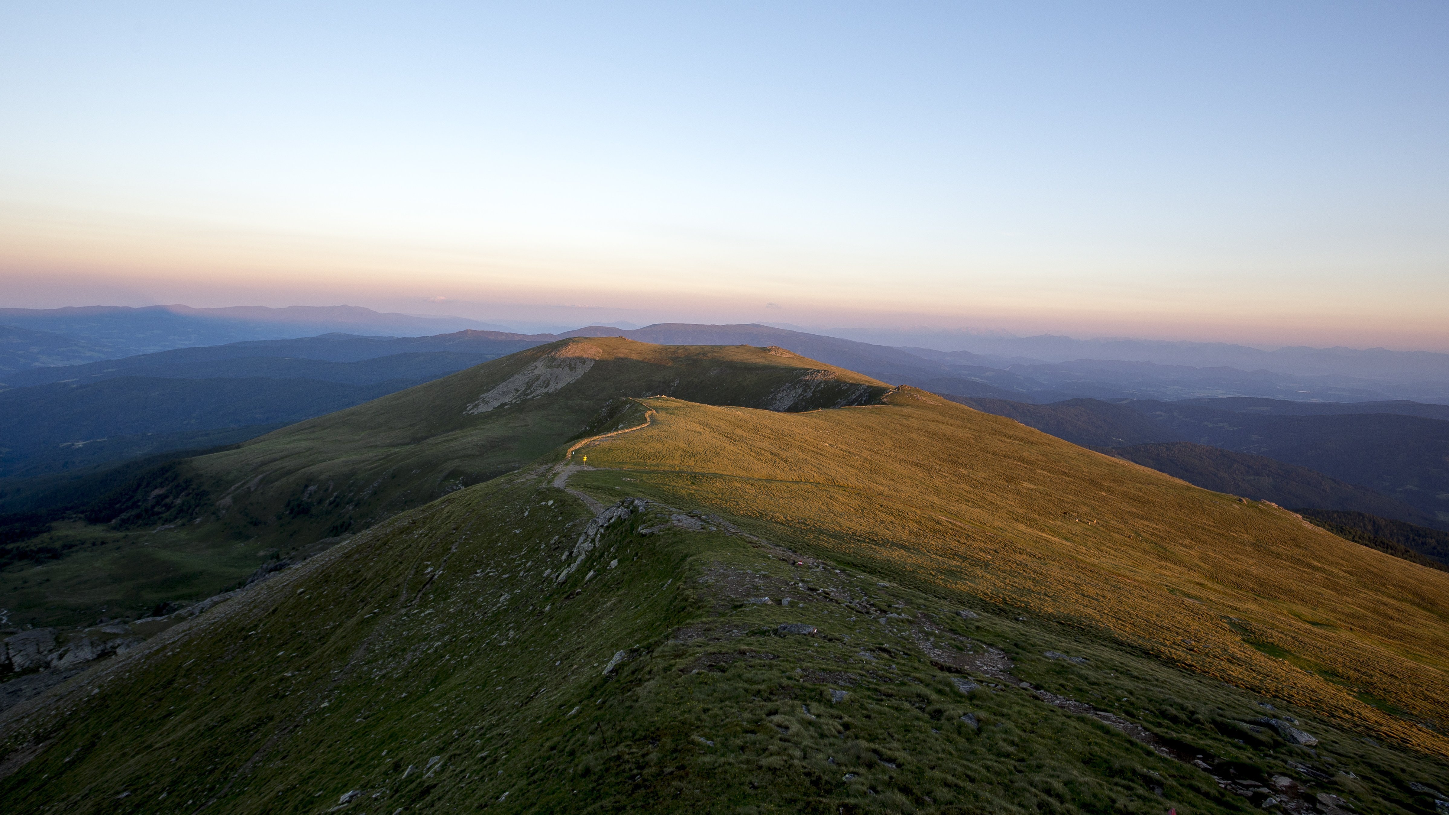 Panoramablick auf die Berglandschaft bei Sonnenuntergang Berglandschaft mit einem Wanderweg und Sonnenuntergang im Hintergrund sichtbar.