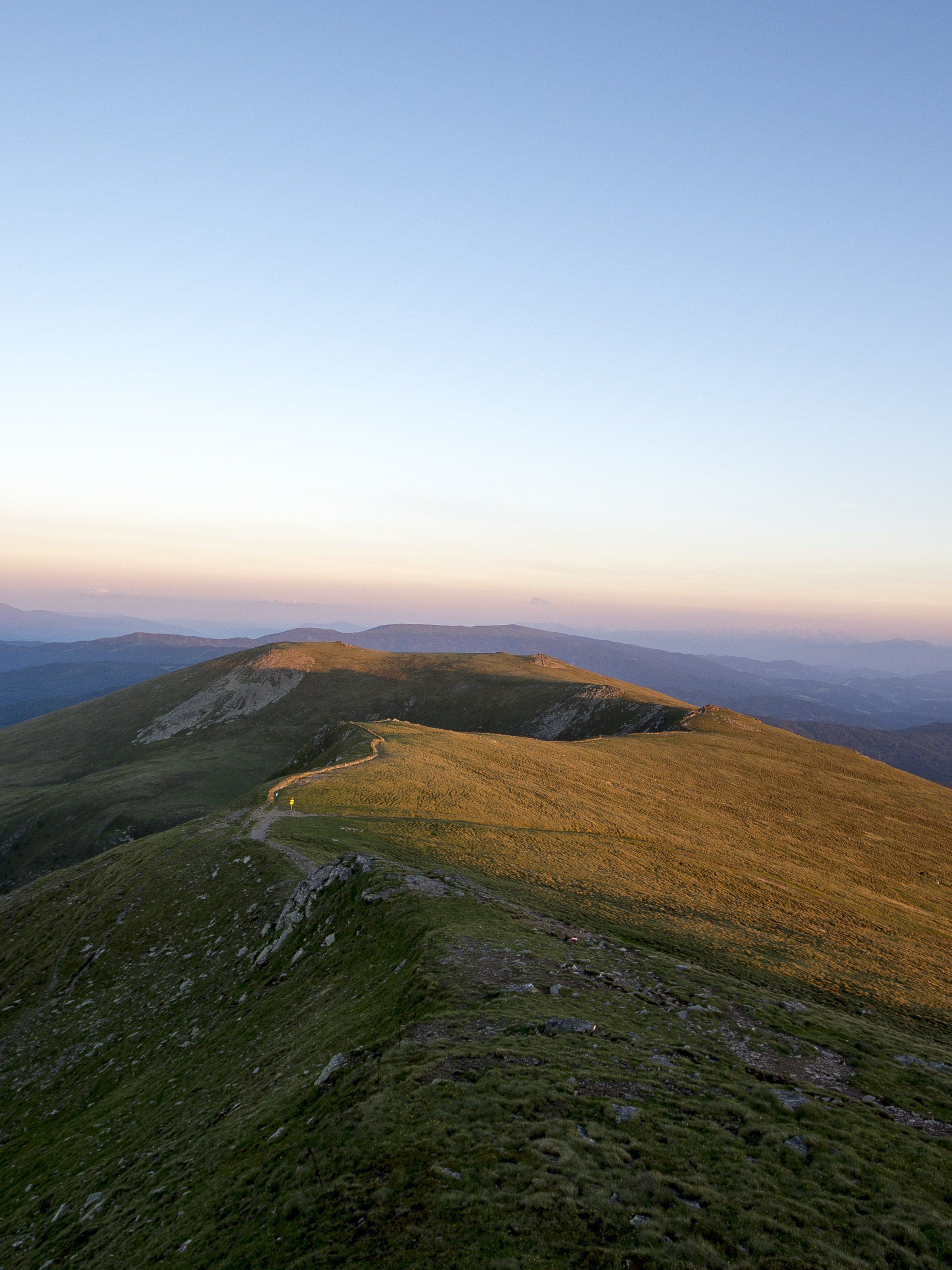 Panoramablick auf die Berglandschaft bei Sonnenuntergang Berglandschaft mit einem Wanderweg und Sonnenuntergang im Hintergrund sichtbar.