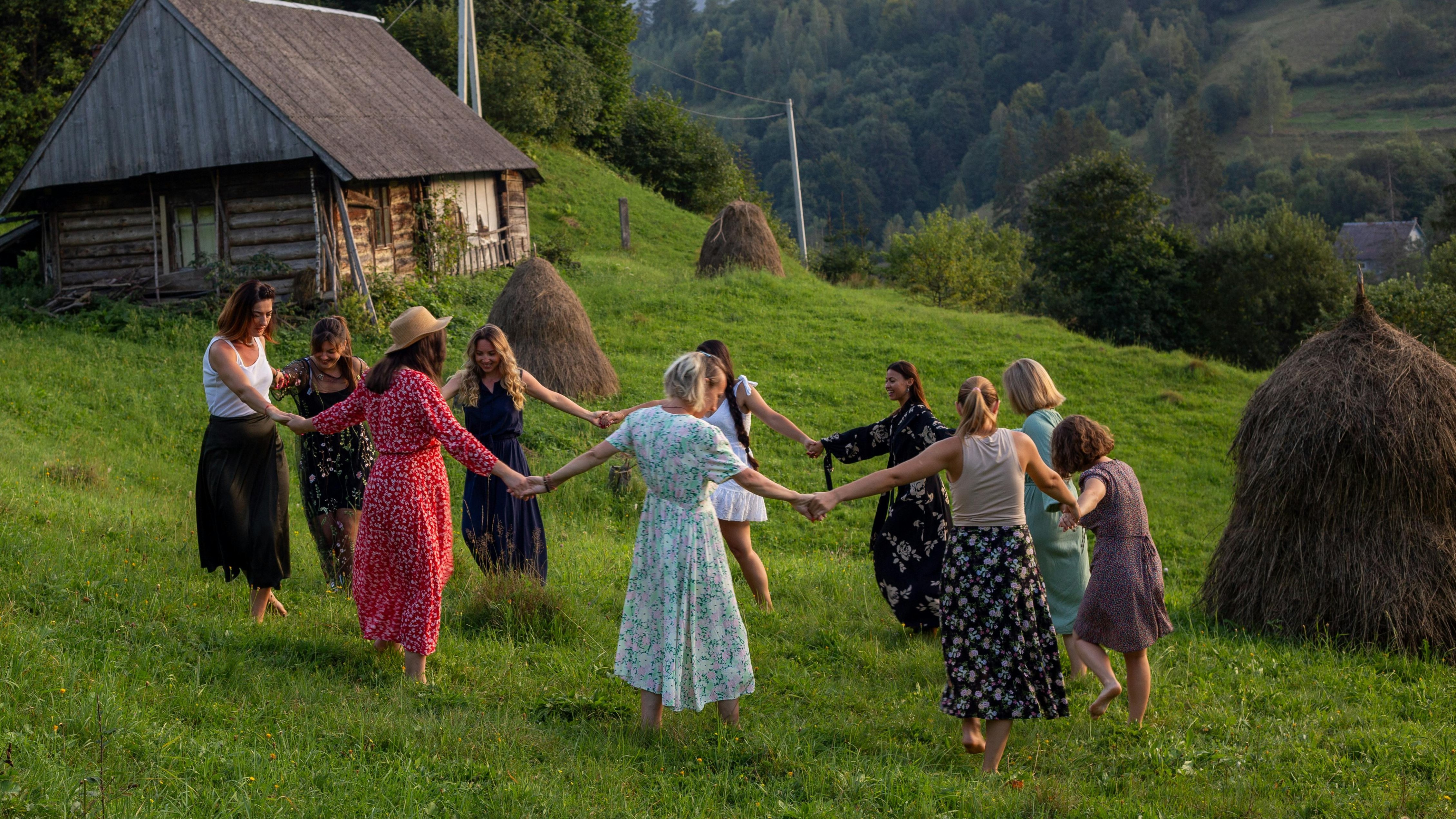 Gemeinschaftliche Feier in der Natur Gruppe von Frauen in traditioneller Kleidung tanzt im Freien auf einer Wiese vor ländlicher Kulisse