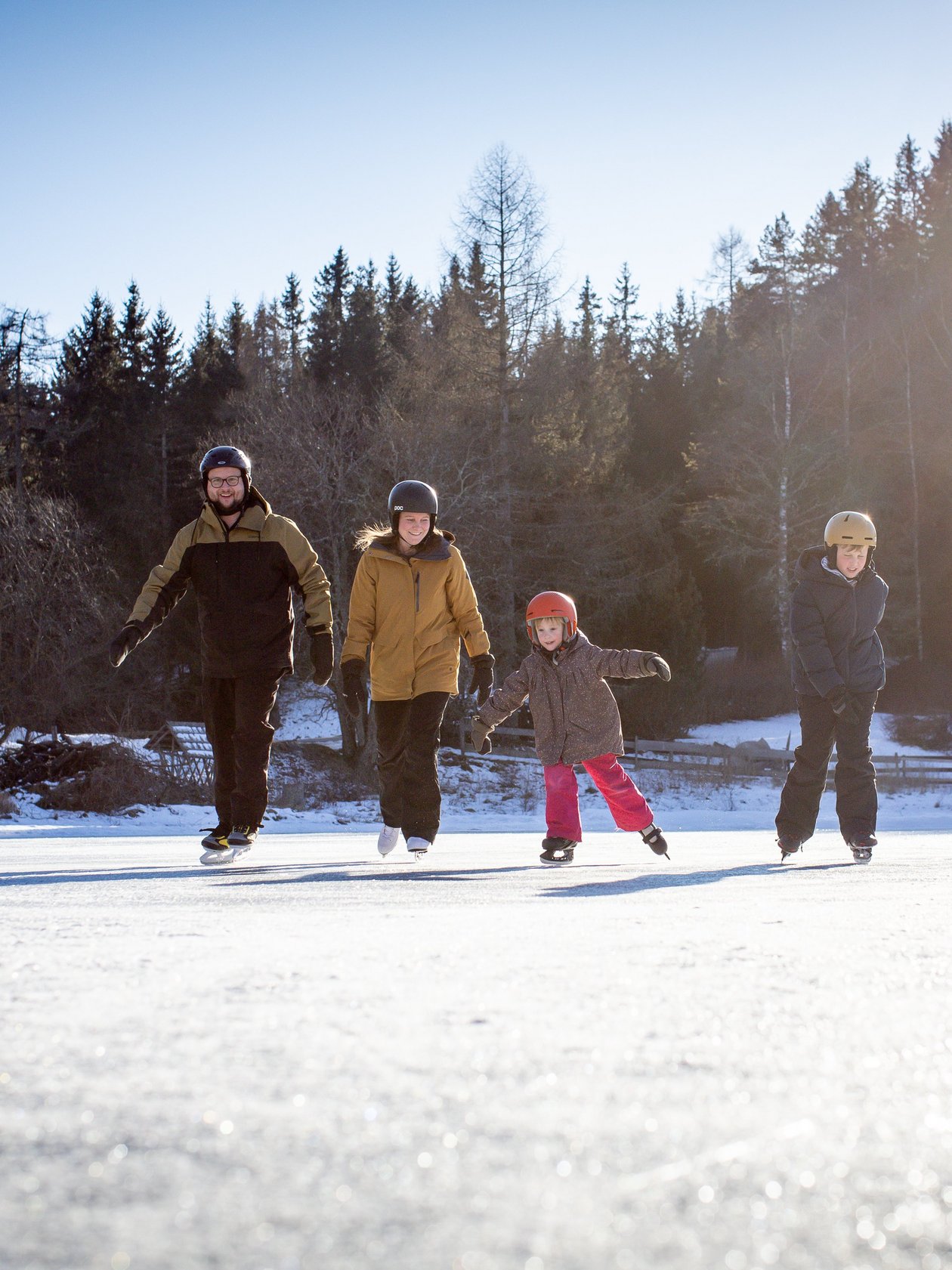 Eislaufen im Winterparadies Familie beim Eislaufen auf einem gefrorenen See umgeben von Bäumen und klarem Himmel