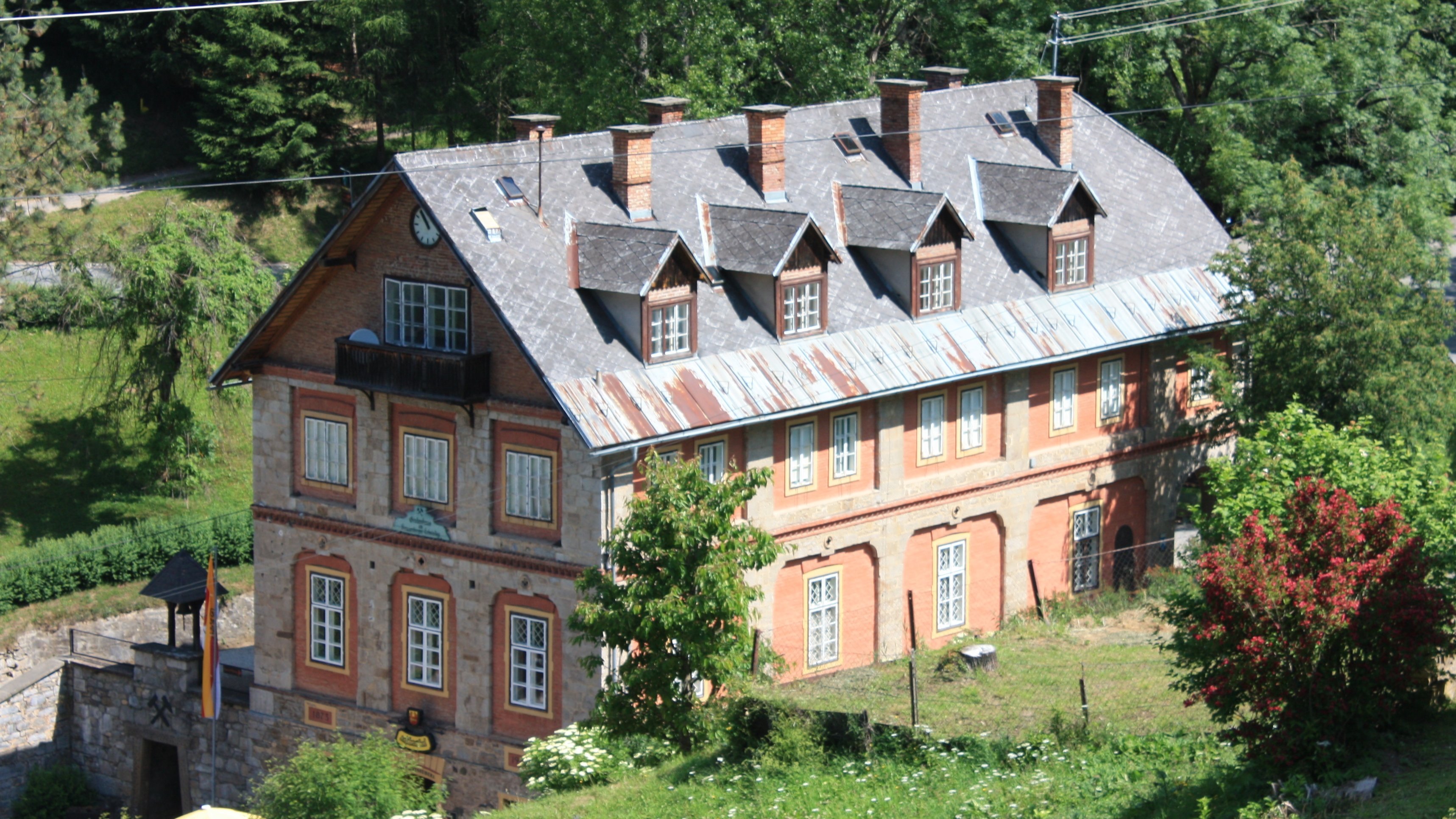 Historisches Backsteingebäude umgeben von Natur Ein historisches Backsteingebäude inmitten üppiger Vegetation mit vielen Fenstern und einem geneigten Dach.