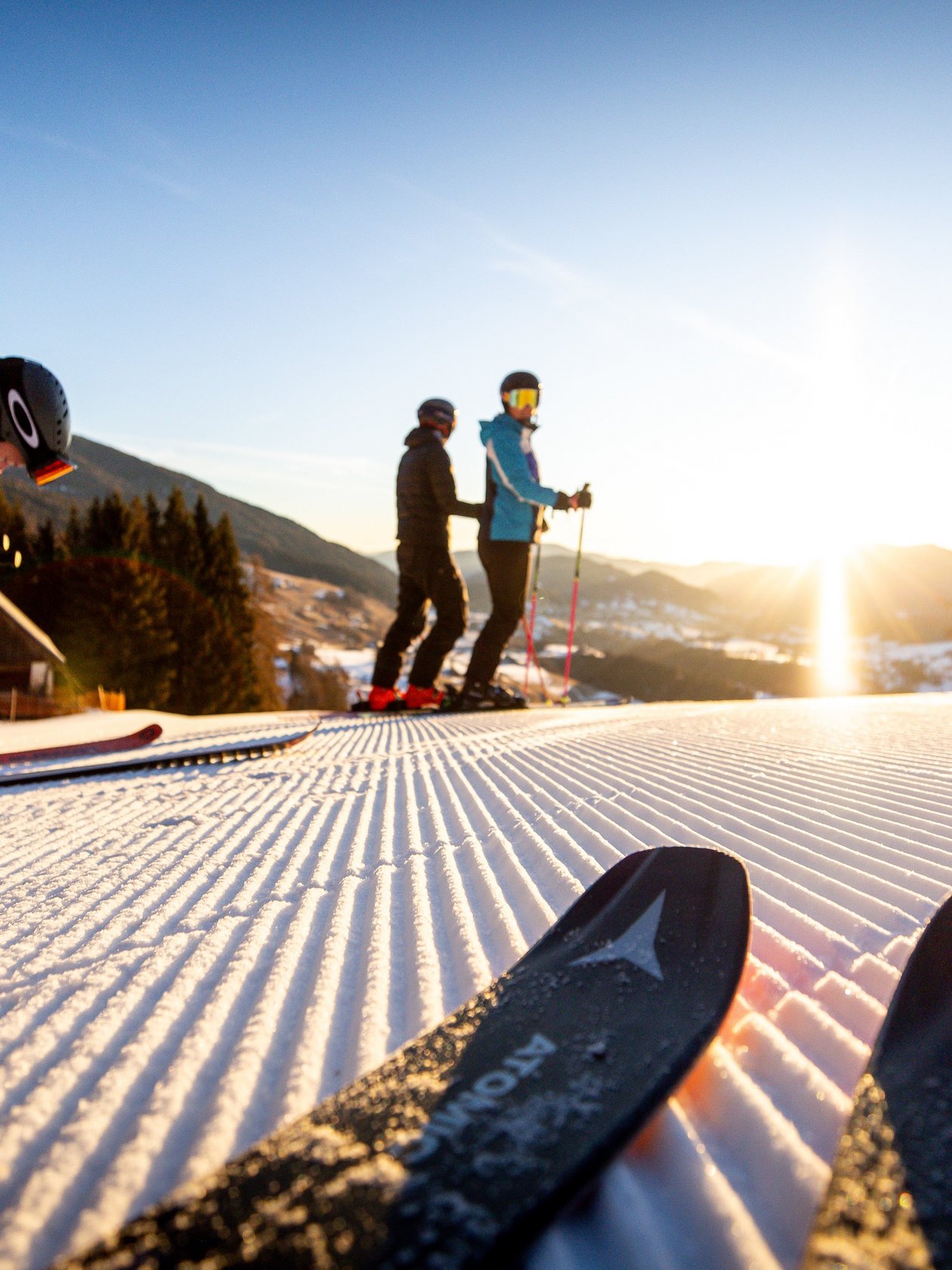 Skifahren im Sonnenuntergang in Murau Drei Skifahrer stehen an einem schneebedeckten Hang in den Bergen zur Abfahrt bereit.