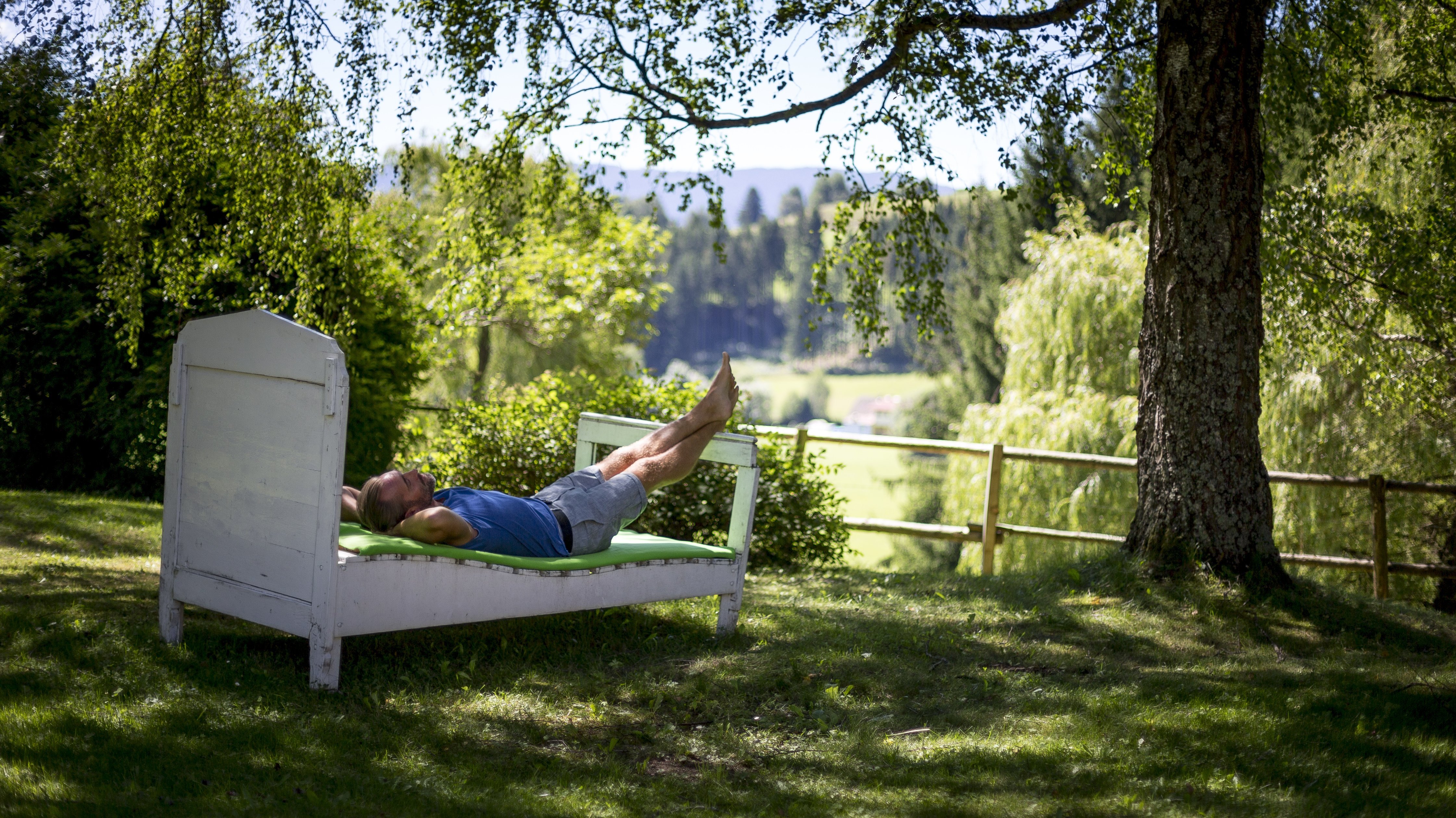 Ruhe im Freien unter Bäumen Person liegt entspannt auf einem Bett im Freien umgeben von Bäumen und Grünflächen.