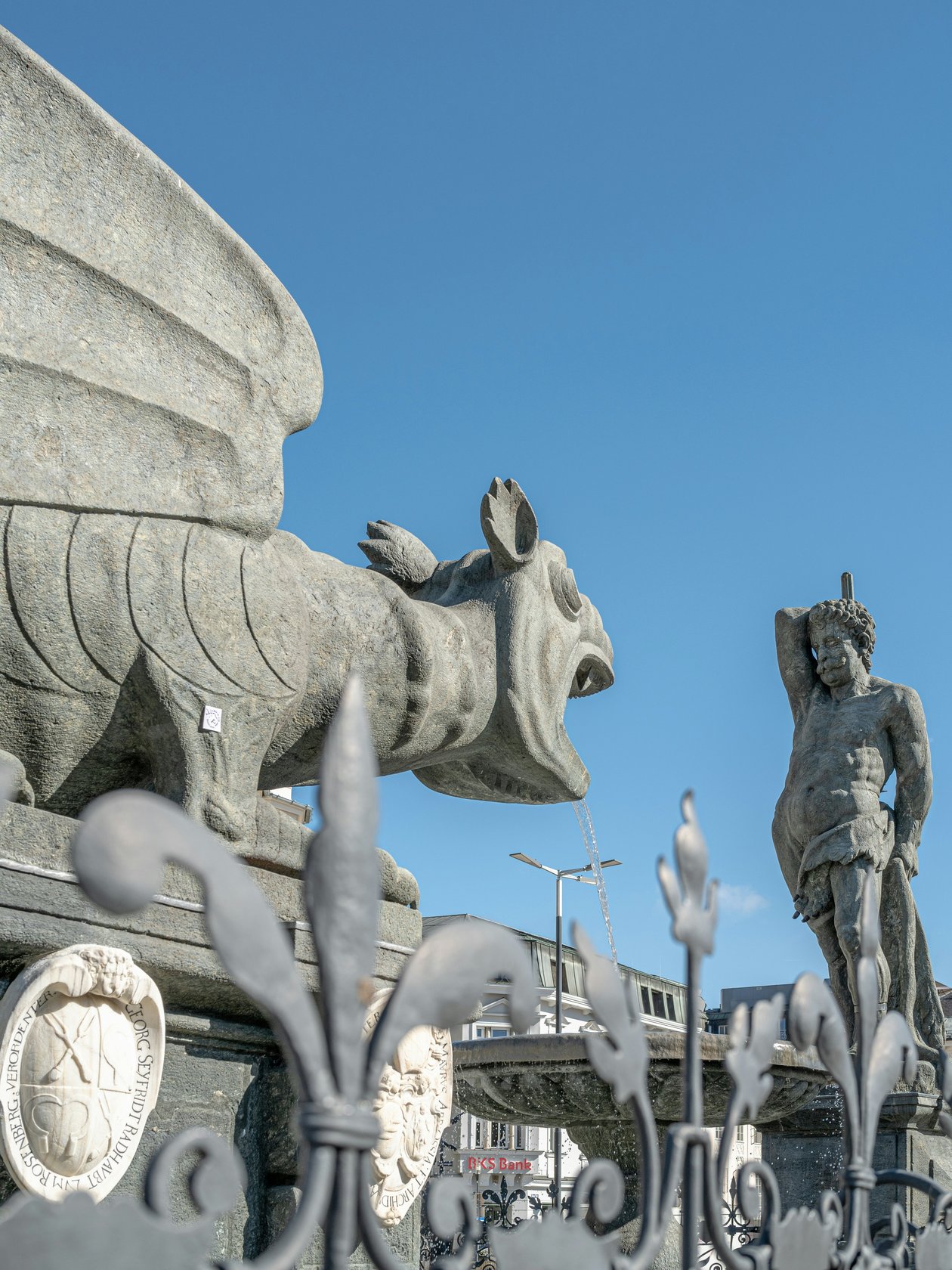Imposante Drachenstatue im Freien Große Drachen-Skulptur neben einer Statue vor blauem Himmel mit kunstvollem Eisenwerk im Vordergrund