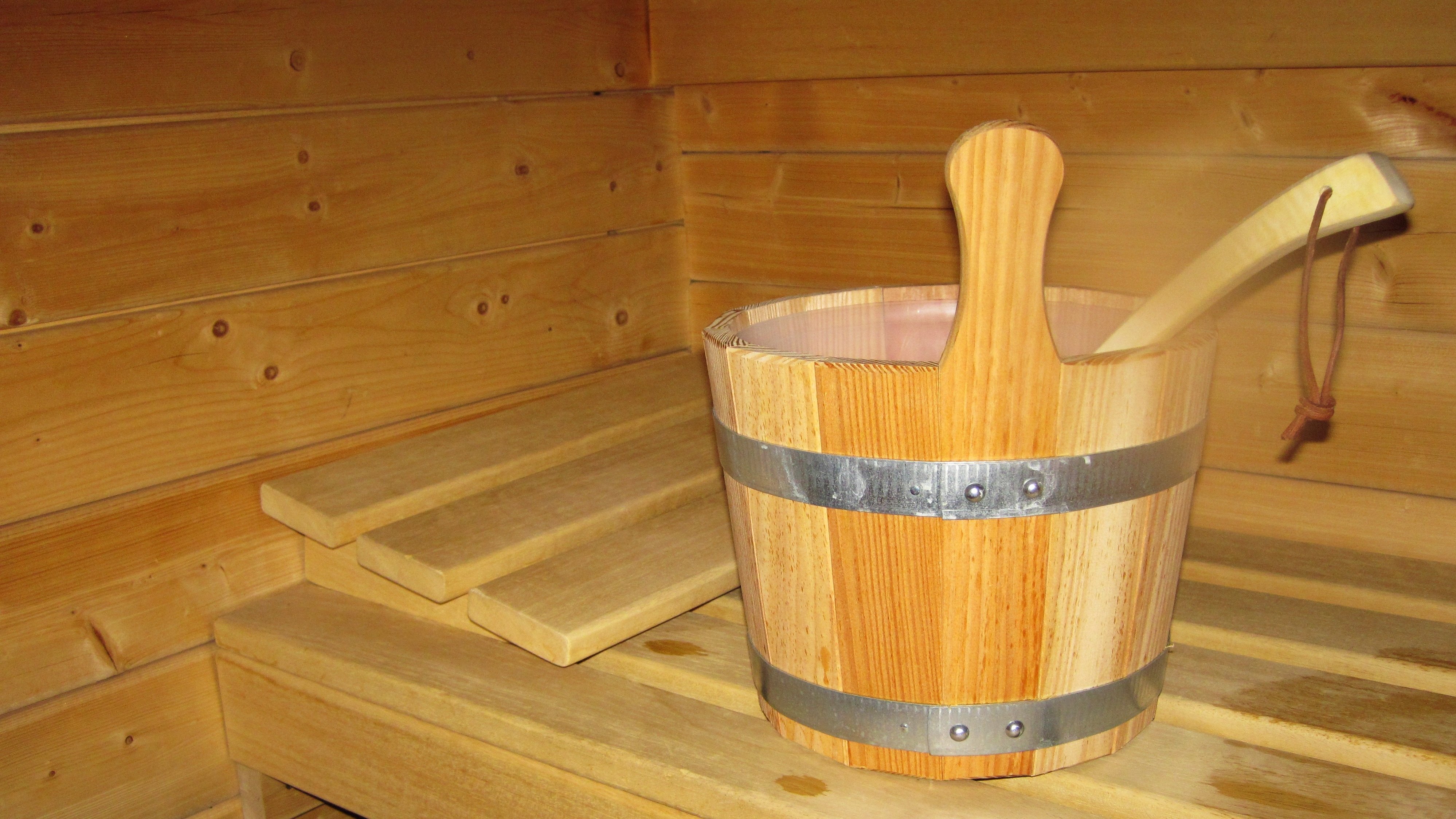 Ein Holzbottich und eine Schöpfkelle auf einer Holzbank in der Sauna mit rustikalen Wänden.
