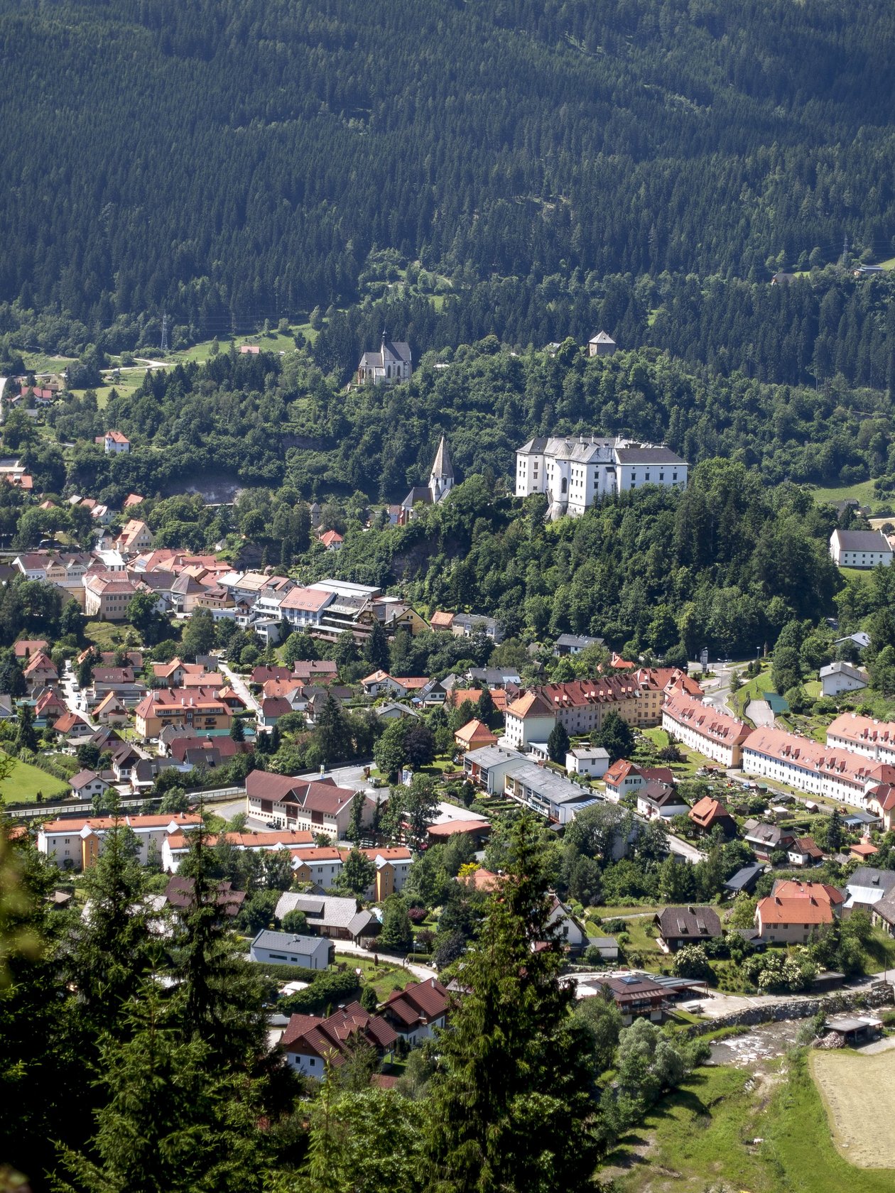 Luftaufnahme eines Bergdorfes umgeben von grüner Landschaft und Hügeln mit sichtbaren Gebäuden