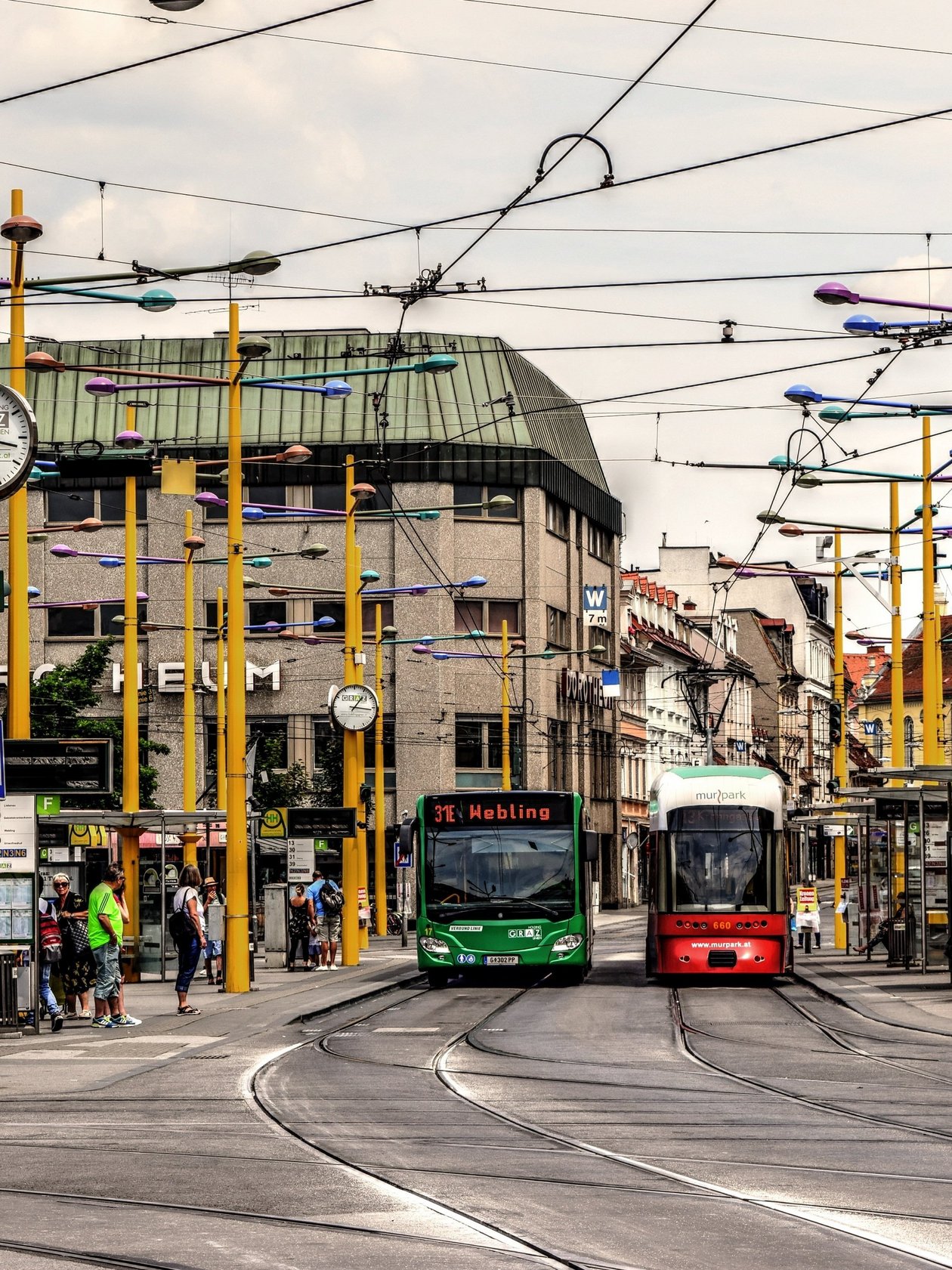 Belebte Tramhaltestelle in urbaner Umgebung Tramstation mit zwei wartenden Straßenbahnen und Menschen an der Haltestelle in einer Stadtlandschaft