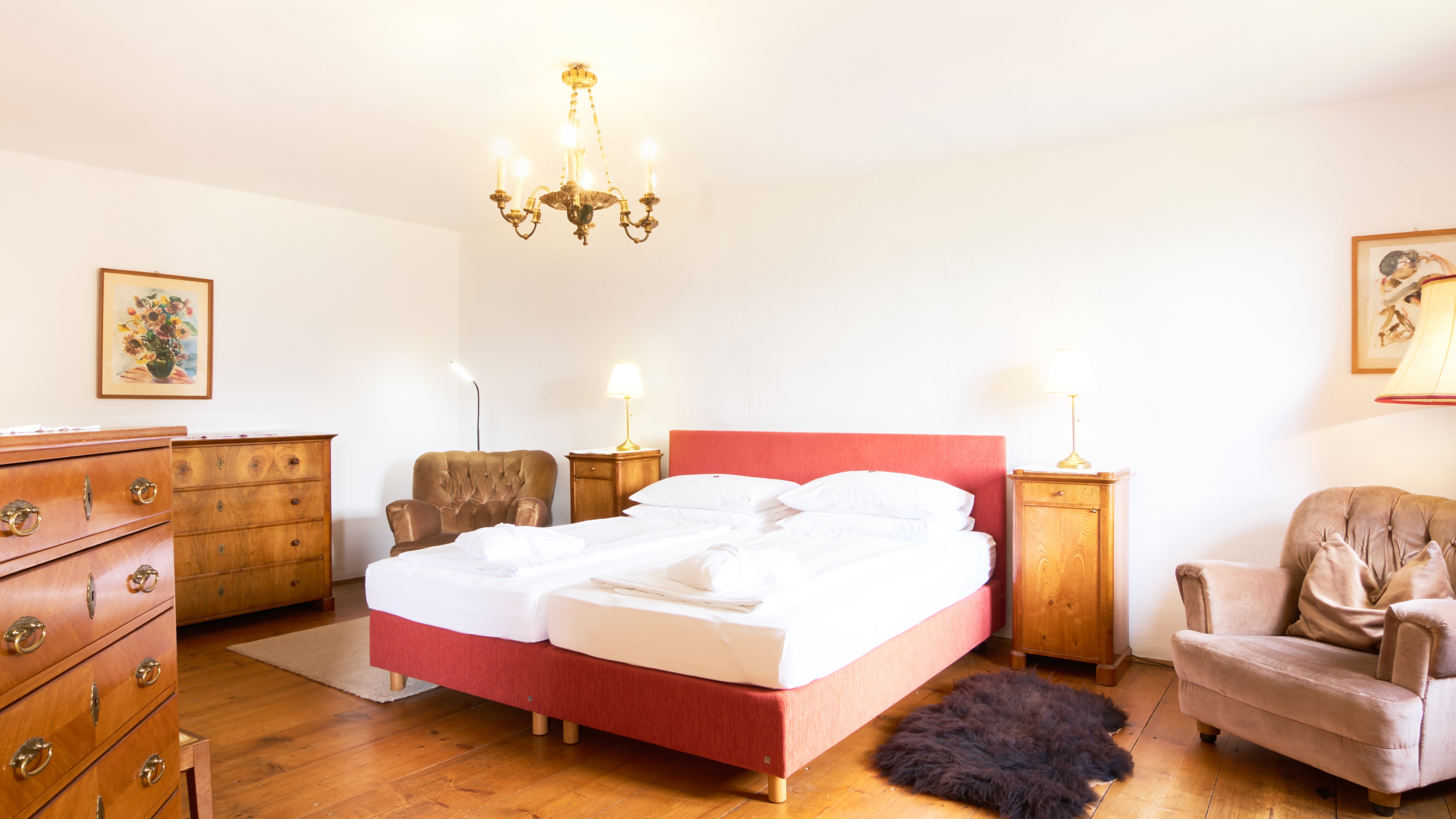 Helles Schlafzimmer mit rotem Bett und Holzfußboden, dekorativen Elementen und stilvollem Lichtdesign