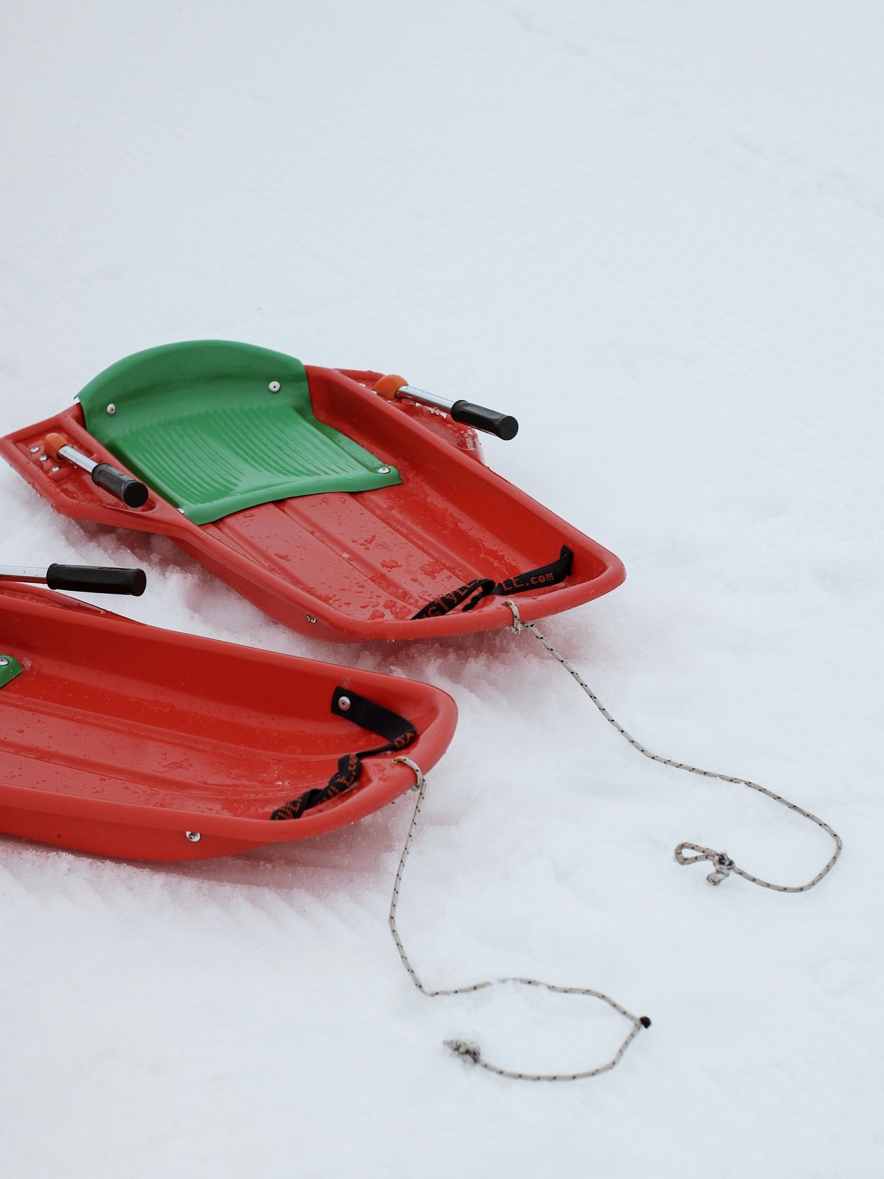 Zwei rote Kunststoffschlitten liegen auf einer schneebedeckten Fläche in der Winterlandschaft