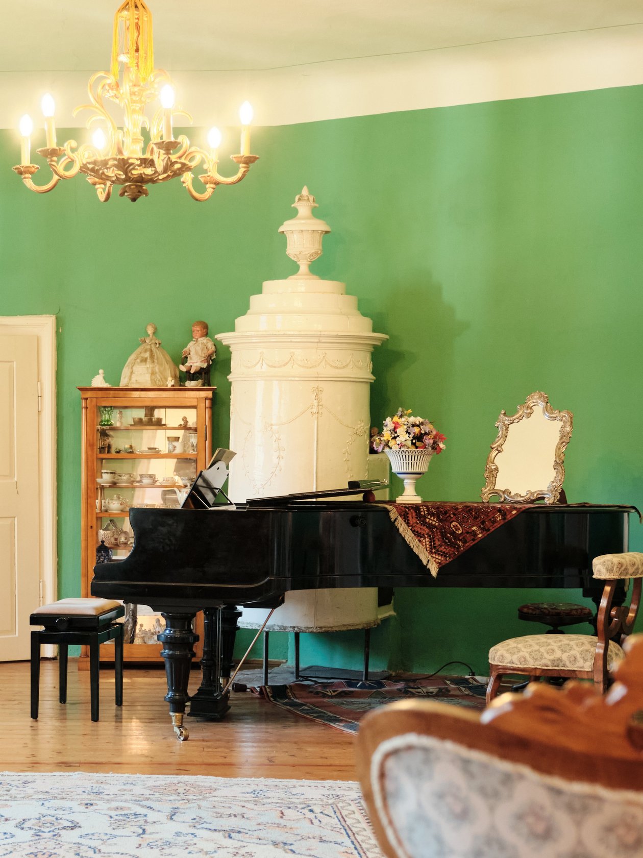 Elegantes Ambiente im Vintage-Stil Vintage Zimmer mit grünen Wänden, Klavier und Kronleuchter zur Dekoration. Es gibt zahlreiche dekorative Elemente.