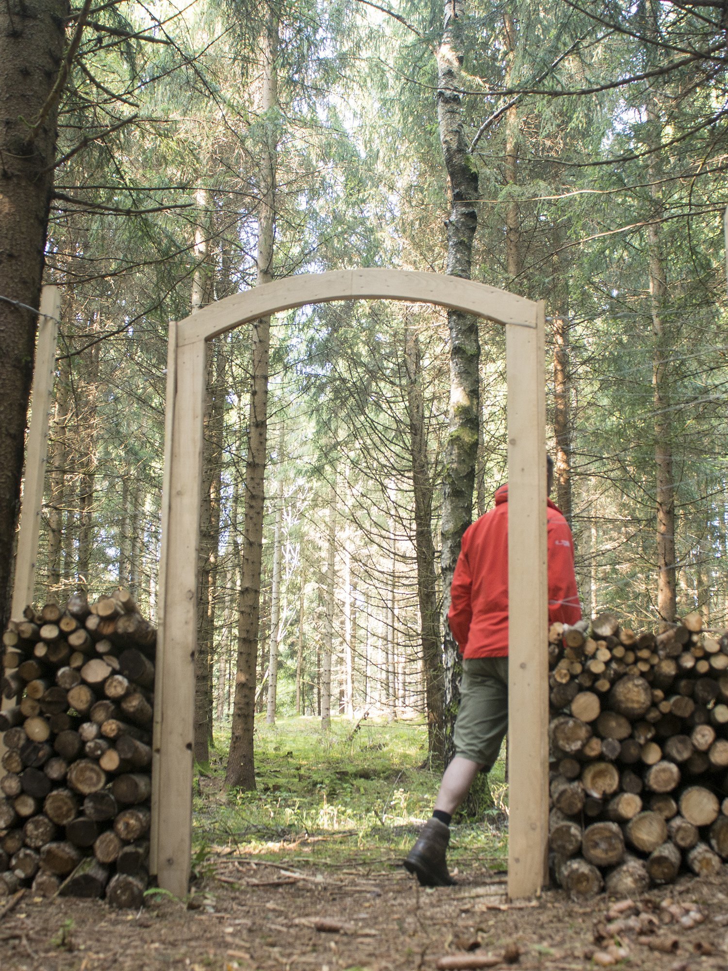 Holzbogen im Wald Person geht durch einen Holzbogen mit Holzstapeln in einem dichten Waldgebiet, umgeben von Natur.