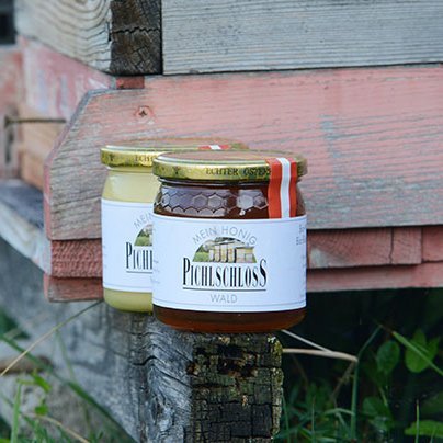 Zwei Honiggläser stehen neben einem Holz-Bienenstock in einer natürlichen Umgebung