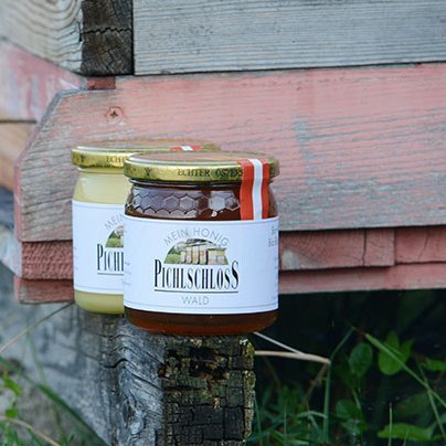 Zwei Honiggläser stehen neben einem Holz-Bienenstock in einer natürlichen Umgebung
