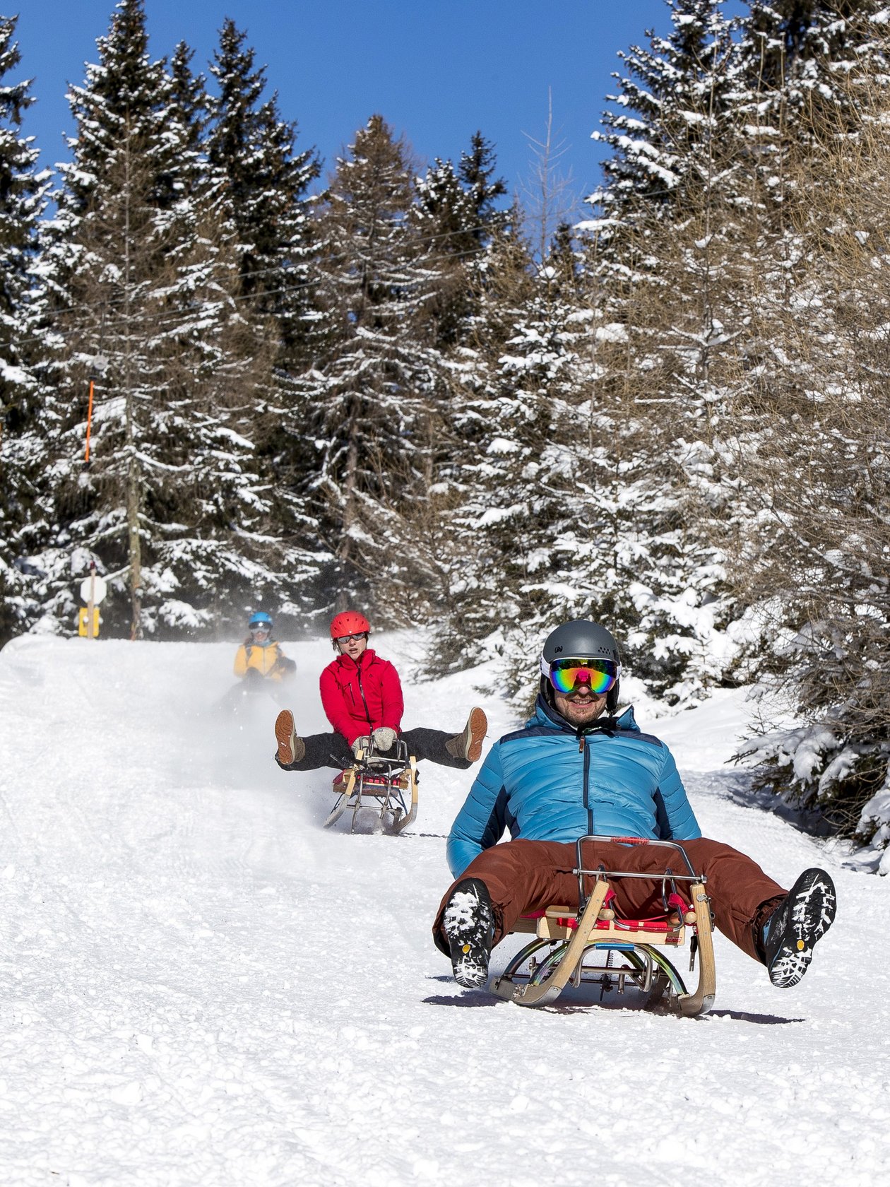Menschen rodeln einen verschneiten Weg in einer winterlichen Landschaft mit Bäumen