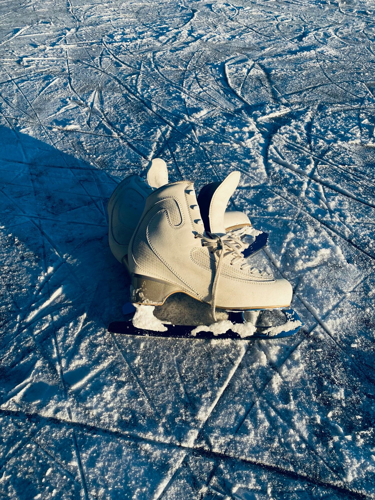 Weiße Eislaufschuhe auf einer schneebedeckten Eisfläche mit Eismustern im Hintergrund