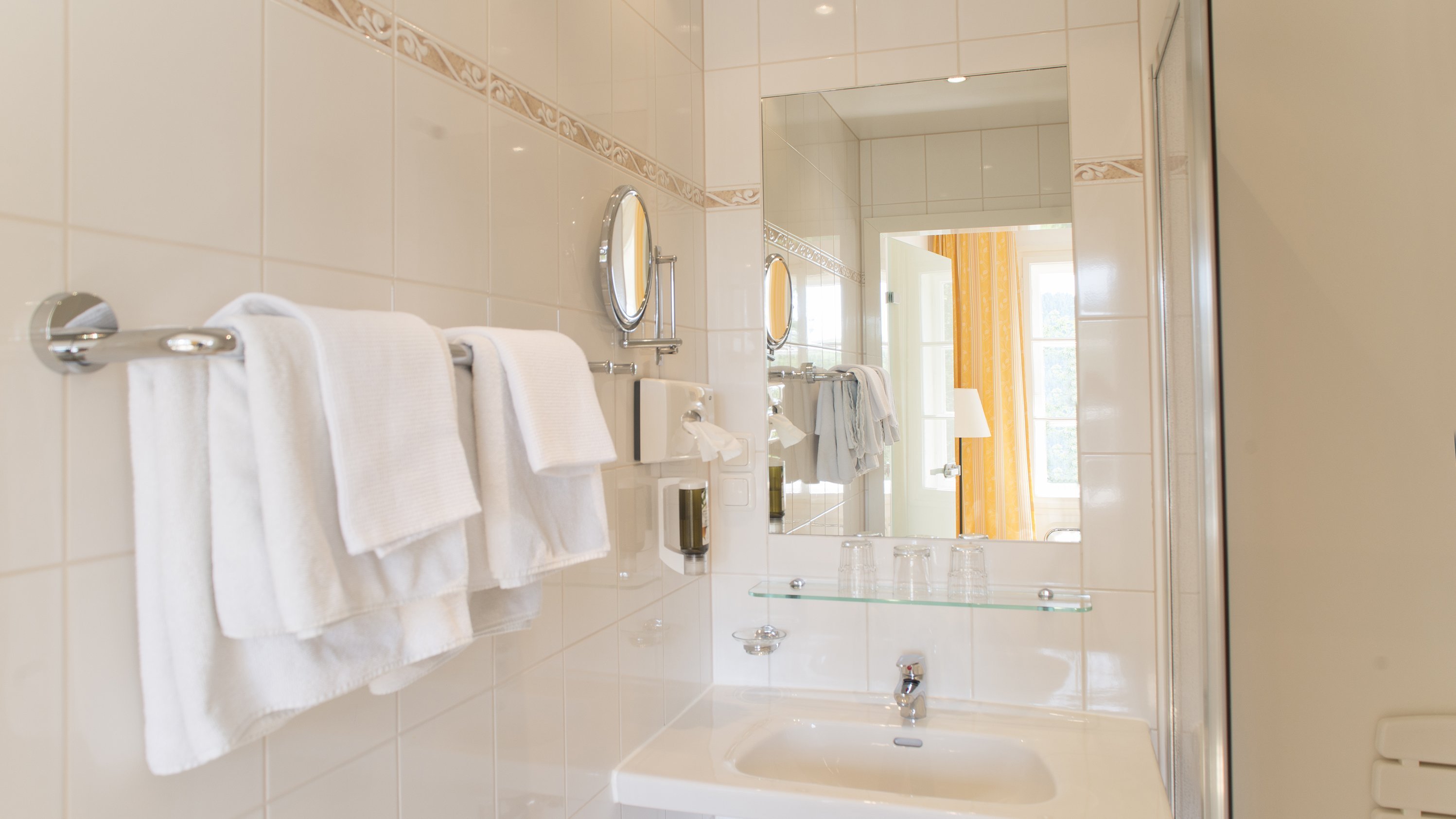Modernes Badezimmer im Hotel Landsitz Pischlschloss Helles Badezimmer mit Waschbecken, Spiegel und ordentlich gefalteten Handtüchern.