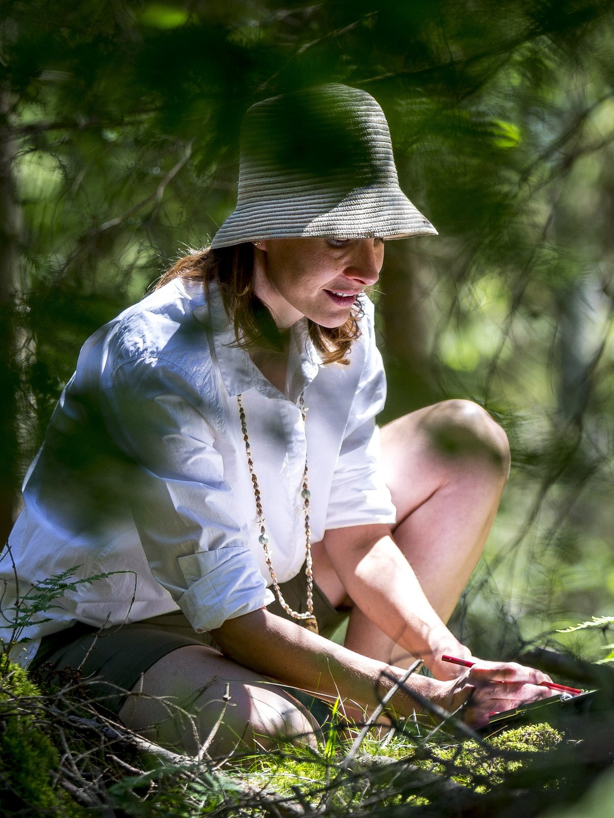 Eine Frau sitzt im Wald und genießt die grüne Umgebung bei einer Aktivität im Freien.