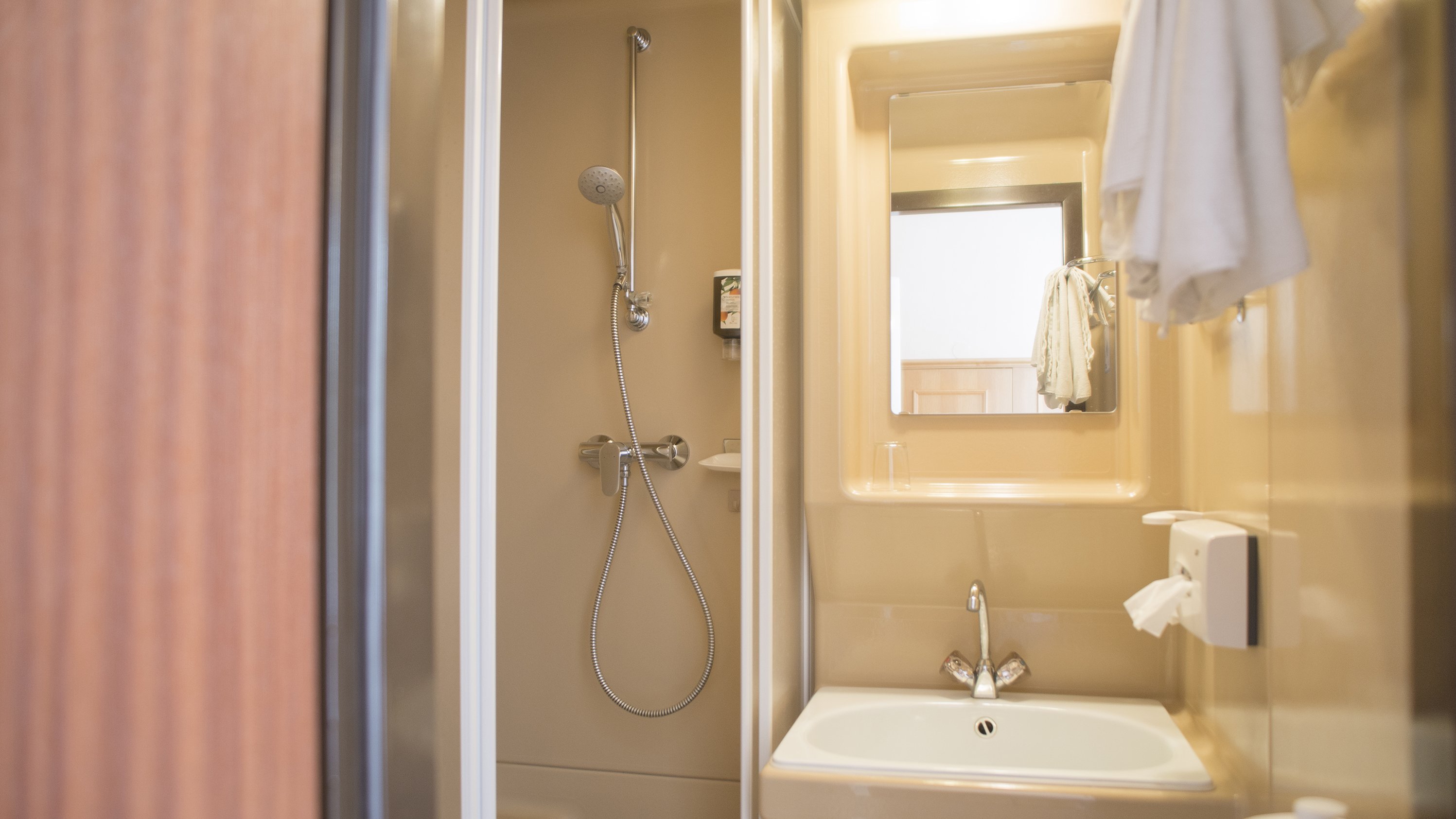 Moderne Badezimmergestaltung im Hotel Kompaktes Badezimmer mit Dusche, Waschbecken und Spiegel in neutralen Farbtönen.