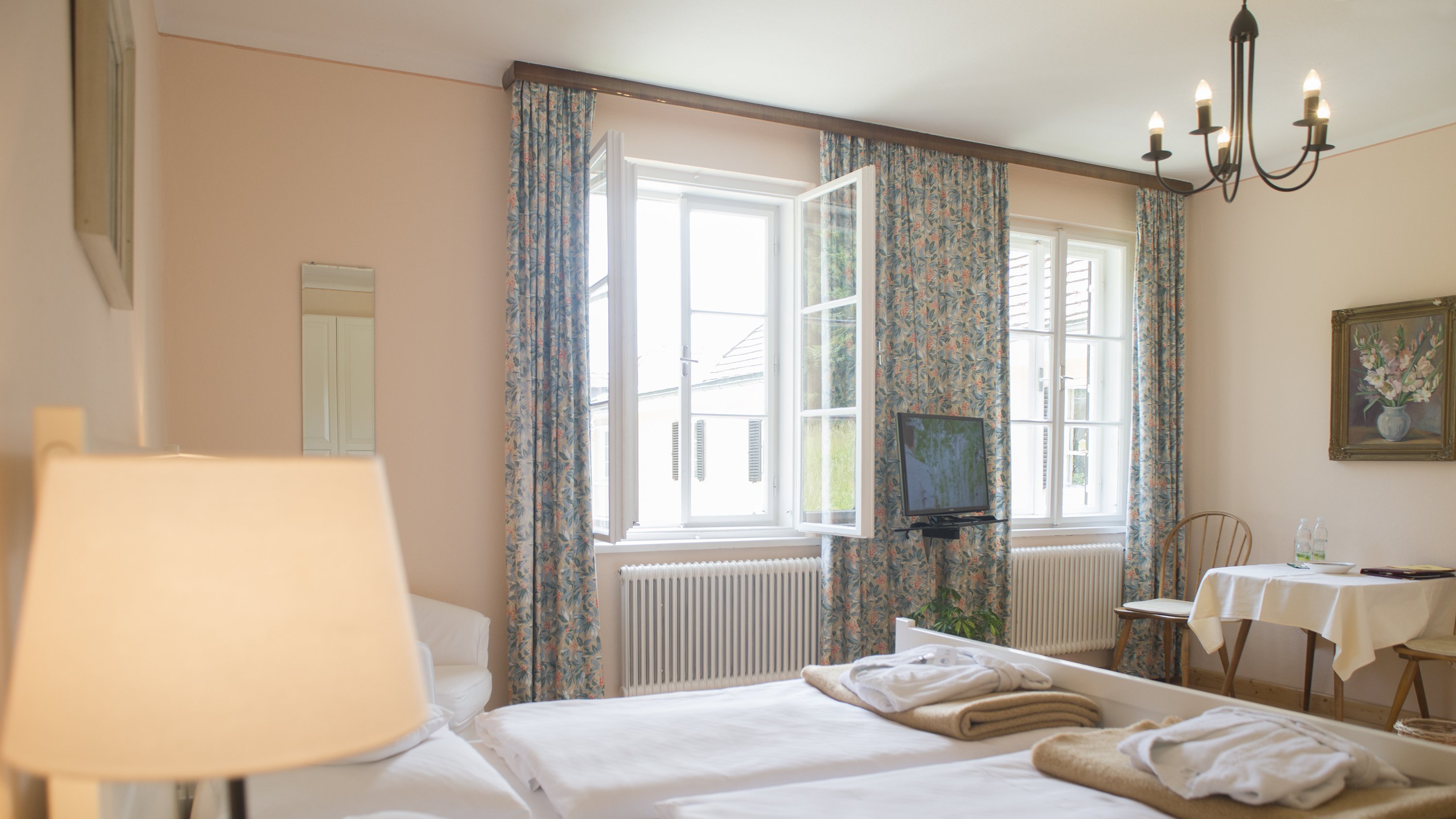 Gemütliches Zimmer mit modernem Design Helle Hotelzimmer mit zwei Betten, einem kleinen Tisch und großen Fenstern mit Blumenvorhängen