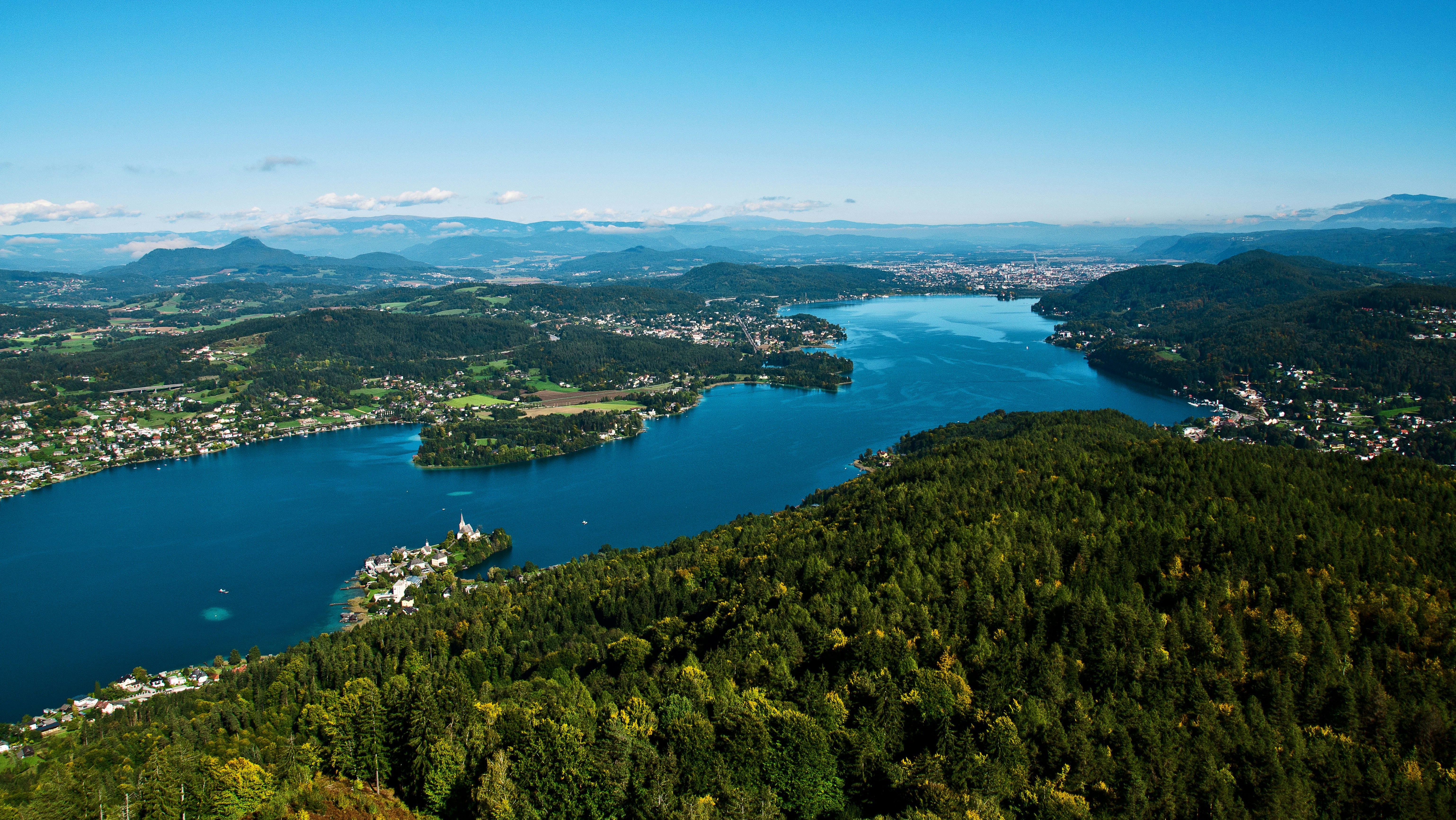 Panoramablick auf den Wörthersee Blick auf einen klaren See umgeben von Bergen und üppigem Grün unter blauem Himmel